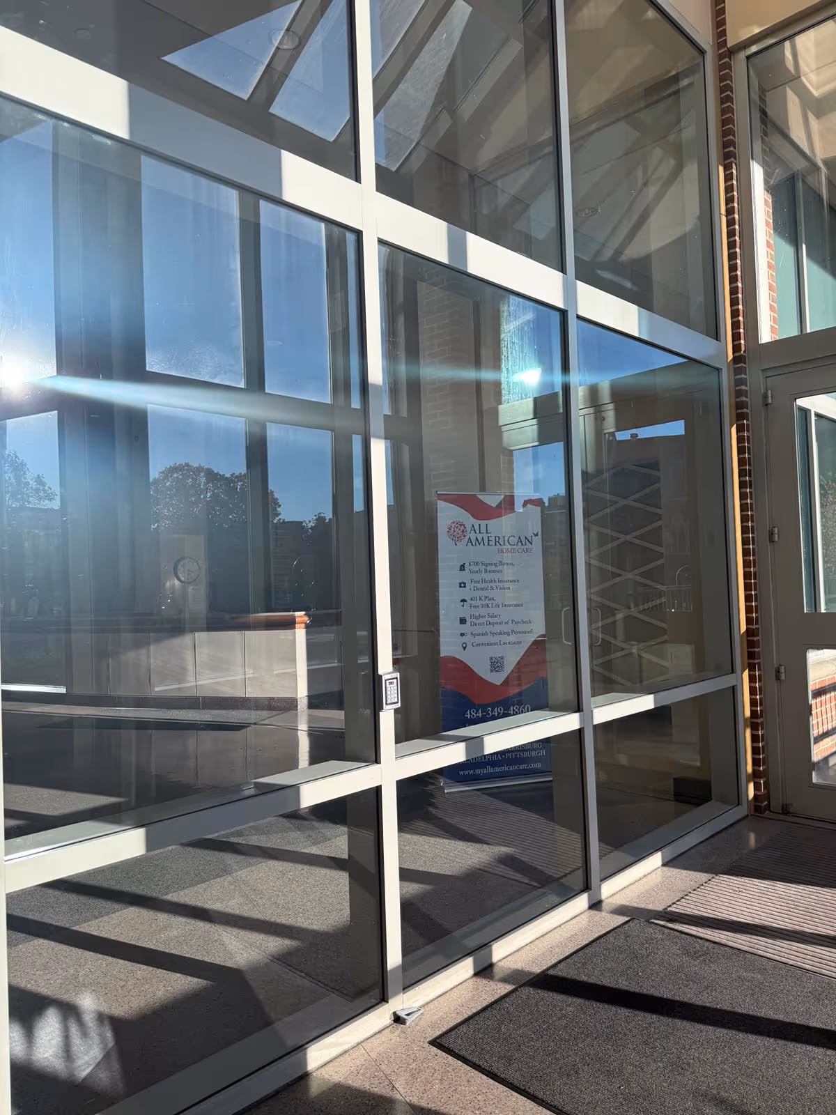 Glass storefront entrance of All American Home Care with a poster inside.