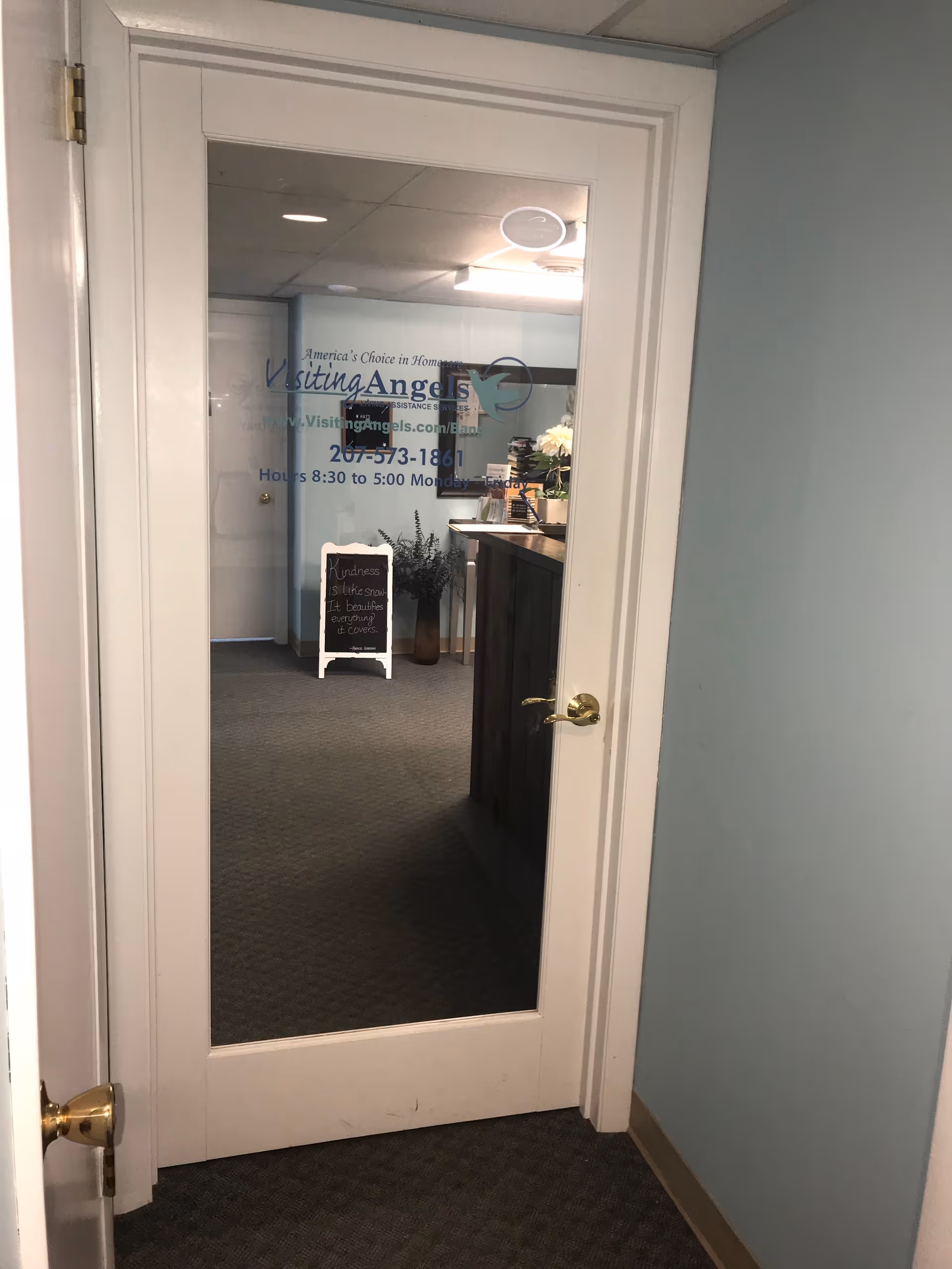 Interior office doorway with glass panel displaying Visiting Angels signage and reception area.