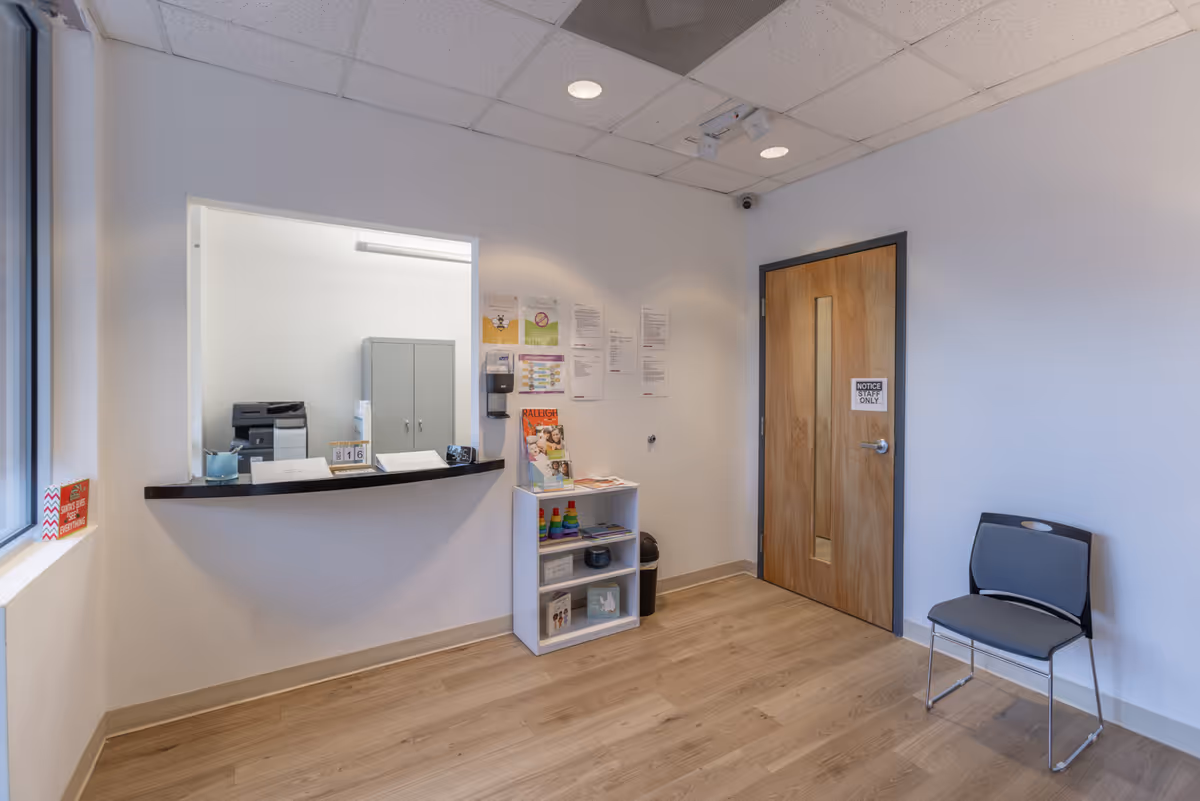 Reception area with a front desk, window, bulletin wall, and a chair.