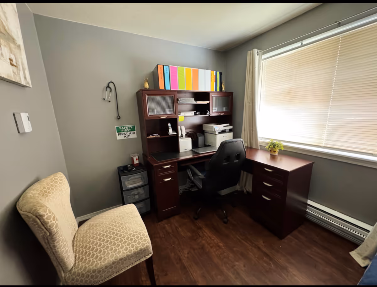Small office with desk, chair, shelves, binders, and a window with blinds.