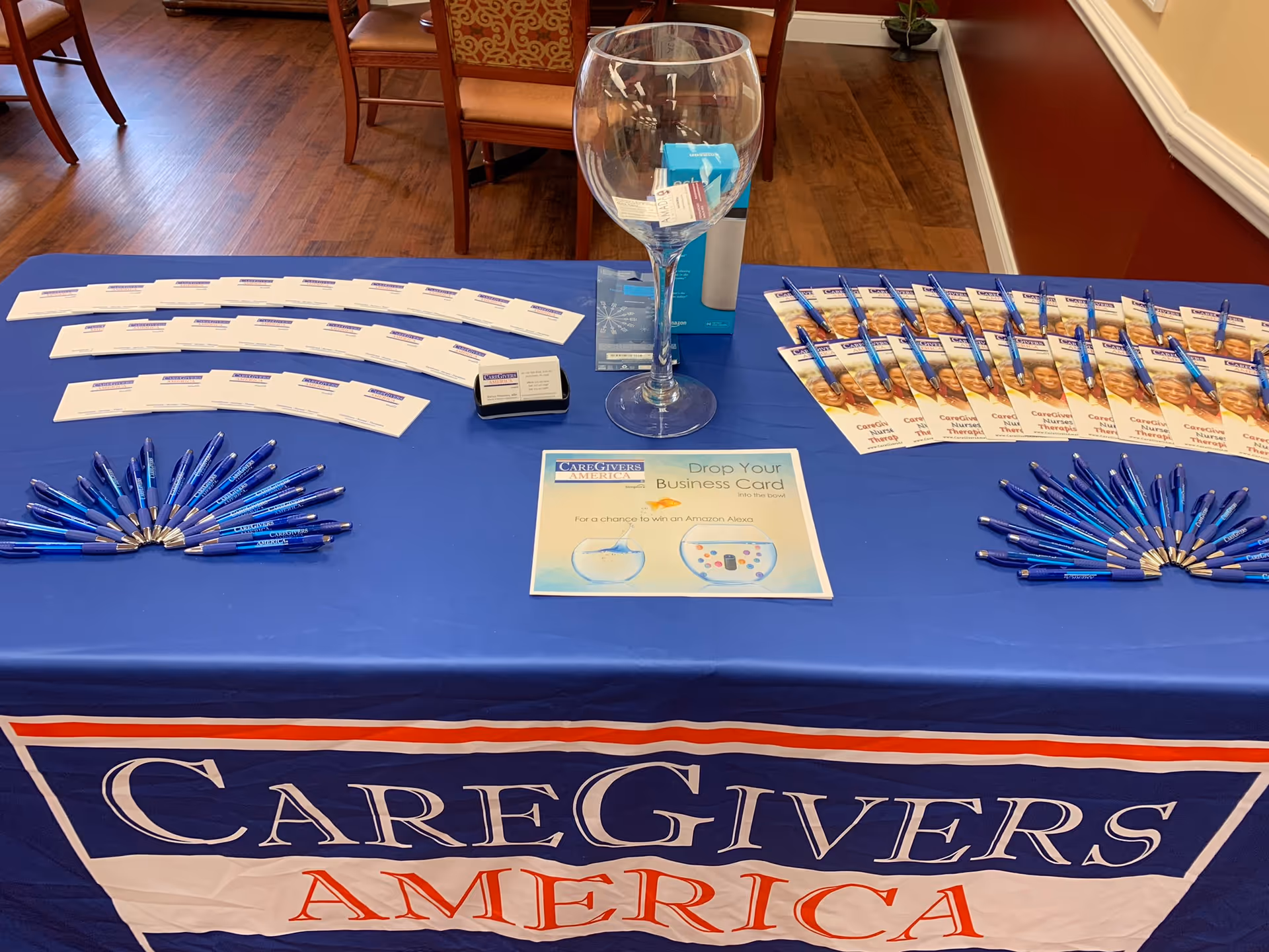 Promotional table indoors with CareGivers America banner, pens, flyers, and a glass centerpiece.