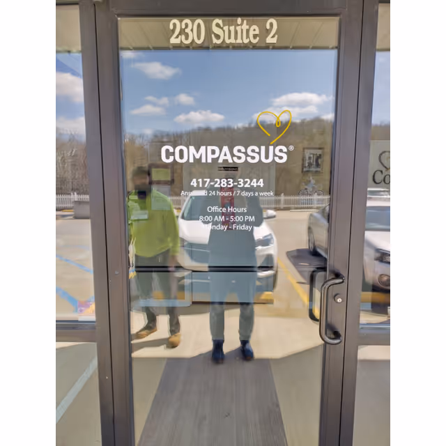 Glass entrance door with Compassus logo and suite number; reflections of people visible.