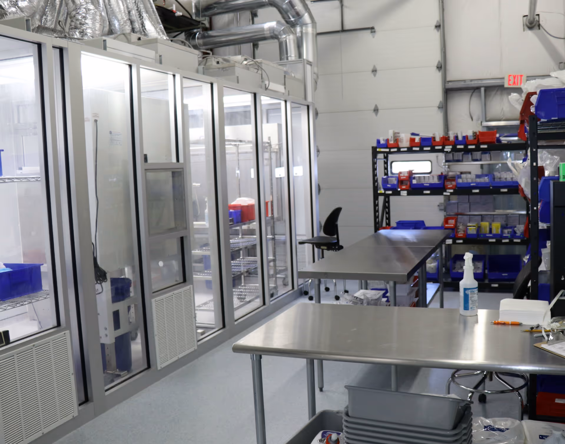 Industrial laboratory with glass-front refrigerators, stainless tables, and organized shelving.