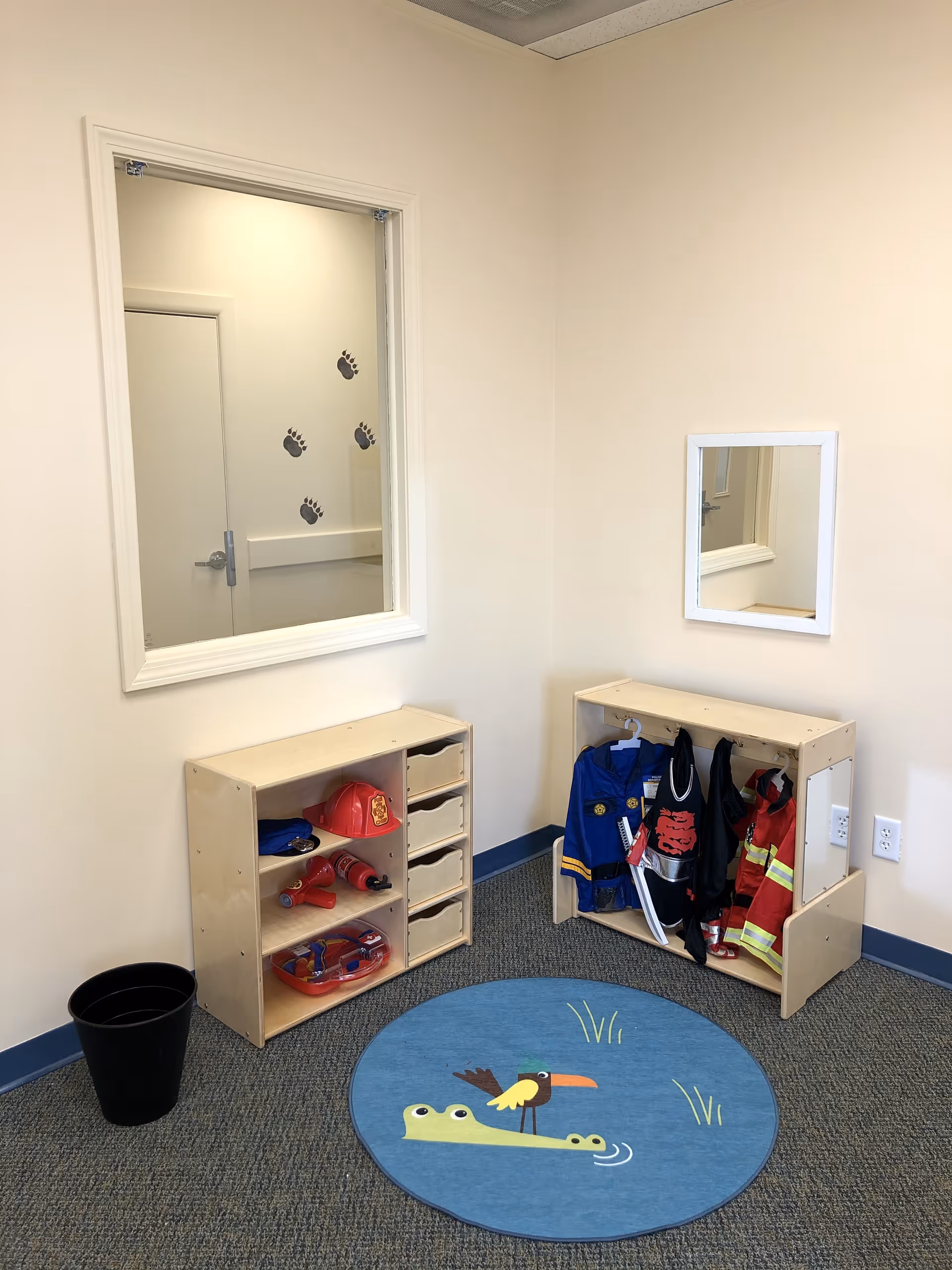 Interior play area with cubbies, dress-up costumes, mirror, and a blue round rug.