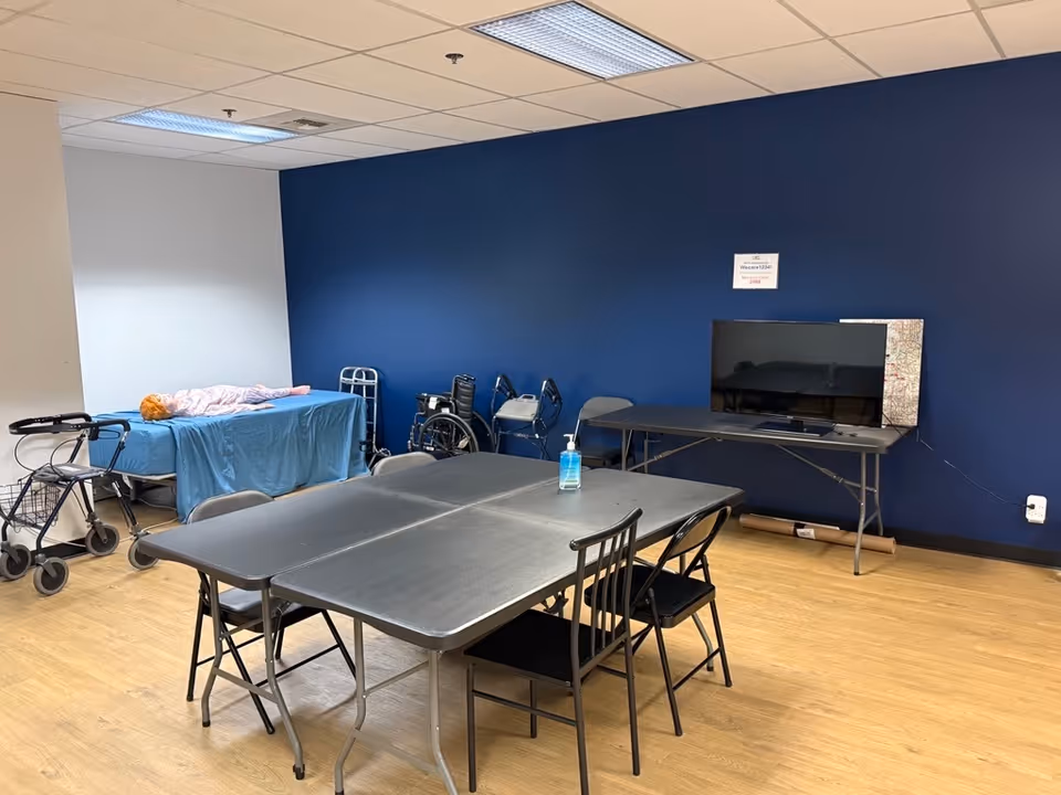 A multipurpose indoor room with a blue wall, tables, chairs, TV, and medical equipment.