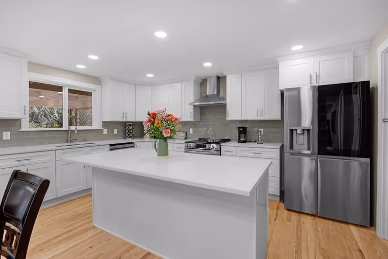 Bright white kitchen in Abby’s Happy Home with island, stainless appliances, and flowers.