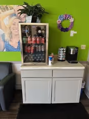 Bright green wall behind a beverage fridge, coffee station, and decorative wreath.