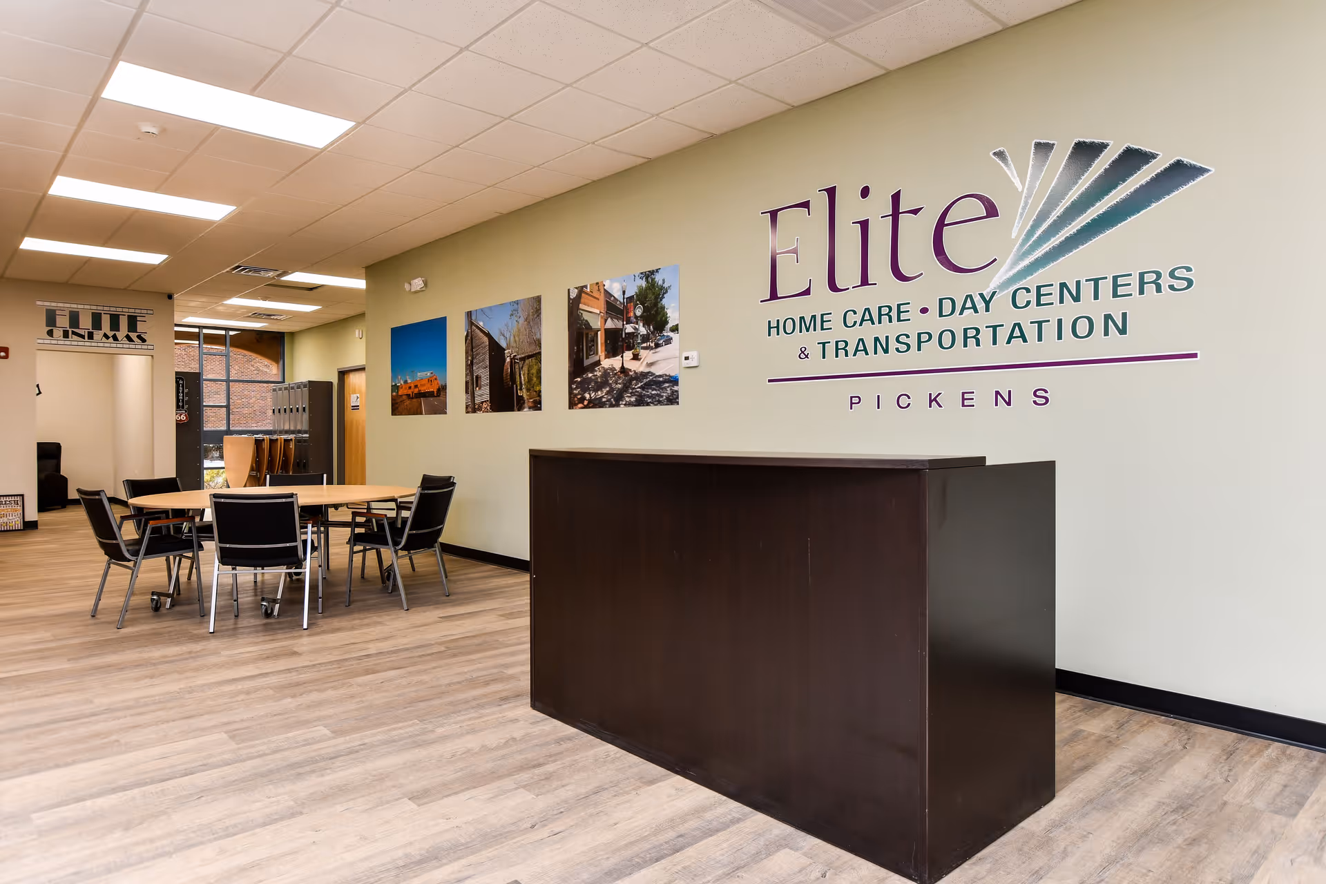 Reception area with dark wooden desk, round tables, chairs, and Elite signage on pale green wall.