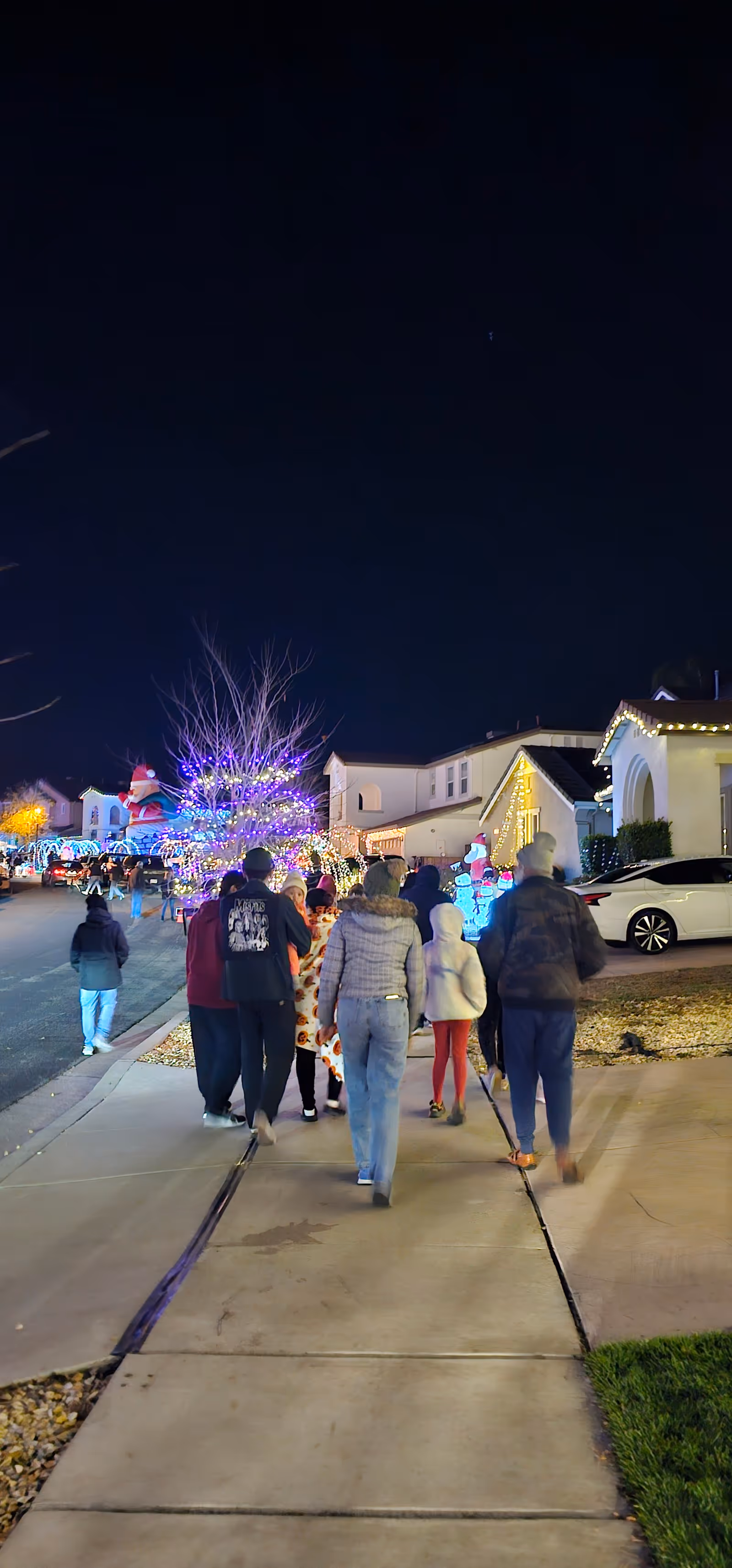 Nighttime outdoor neighborhood sidewalk with people walking past festive holiday lights