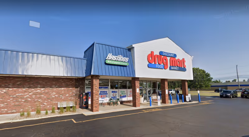 Exterior view of Discount Drug Mart storefront with blue awning and parking lot.