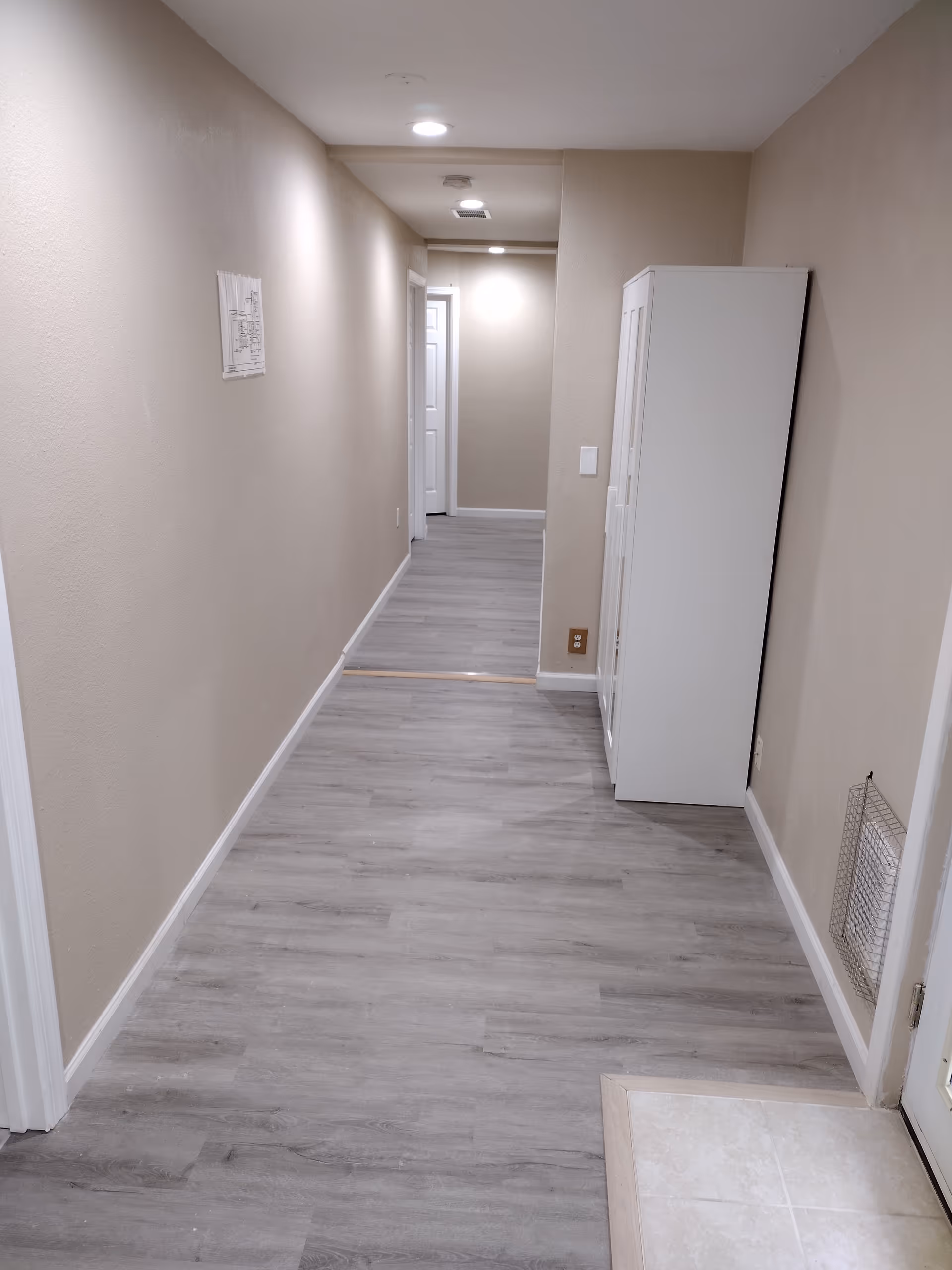 Long hallway in a senior living facility with beige walls and laminate flooring.