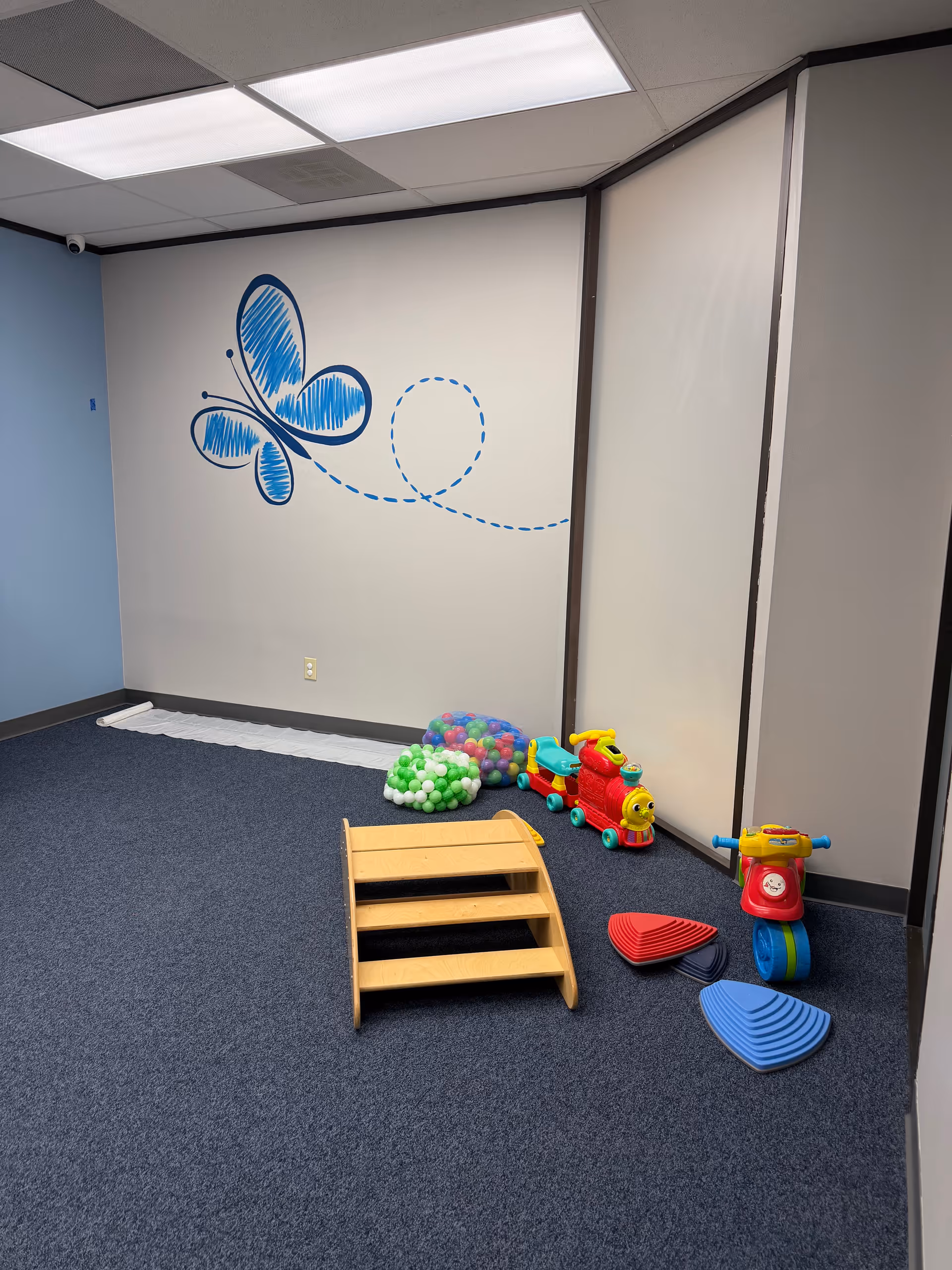 Indoor playroom with a butterfly mural, a small wooden ramp, and colorful ride-on toys.