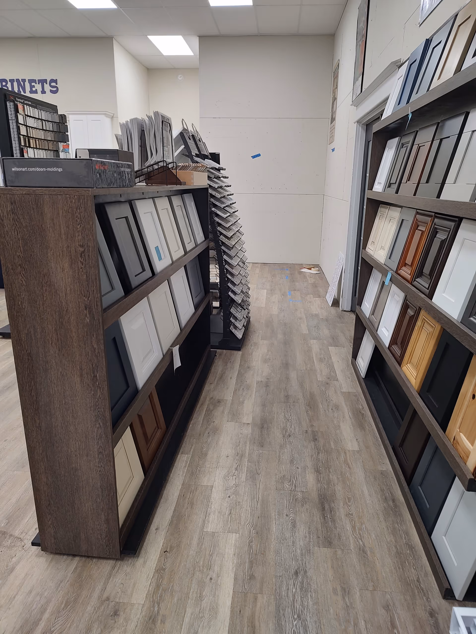 Narrow showroom aisle lined with display cabinet doors and framed samples on shelves