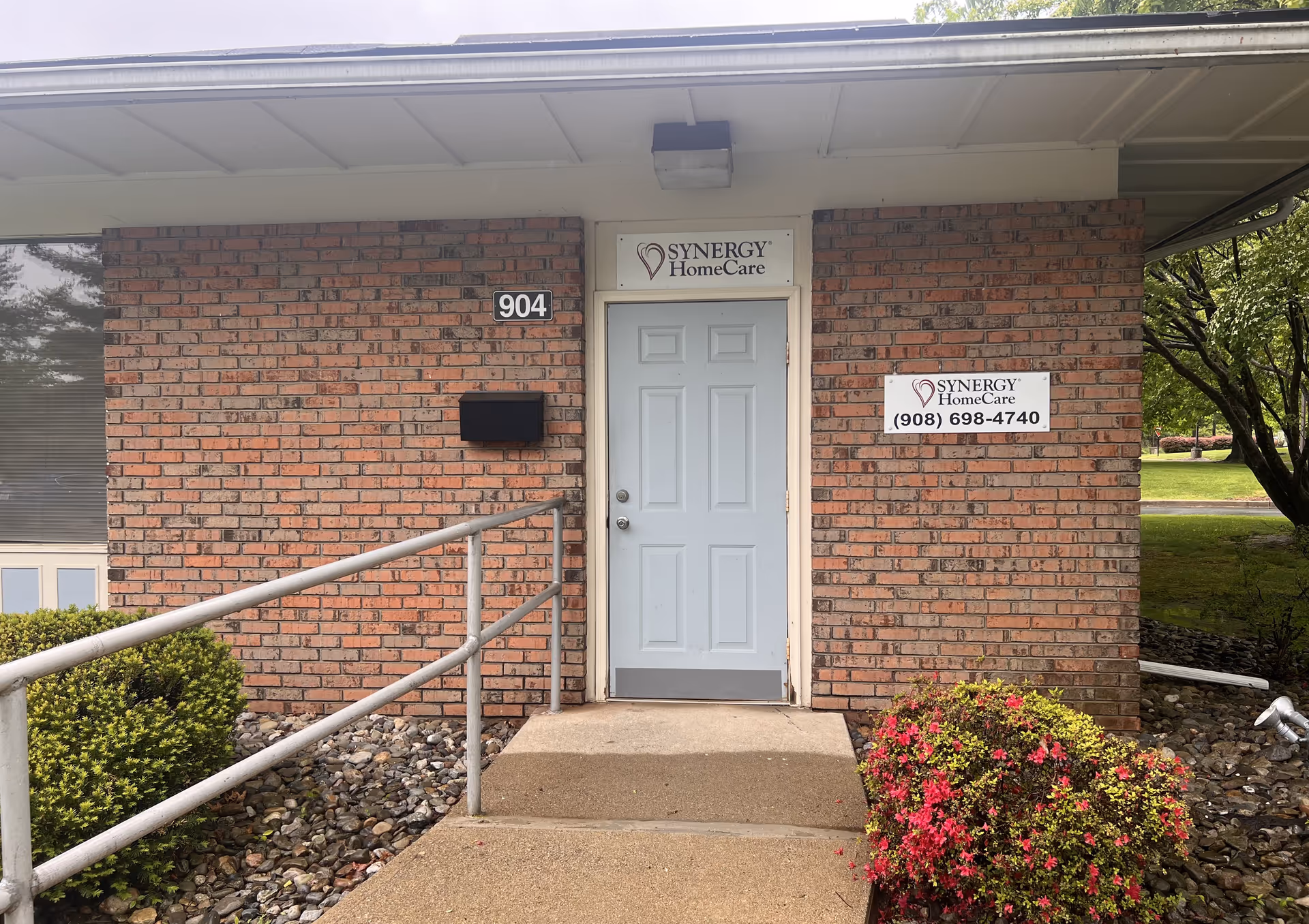 Brick building entrance with a white door, ramp, and Synergy HomeCare signage.