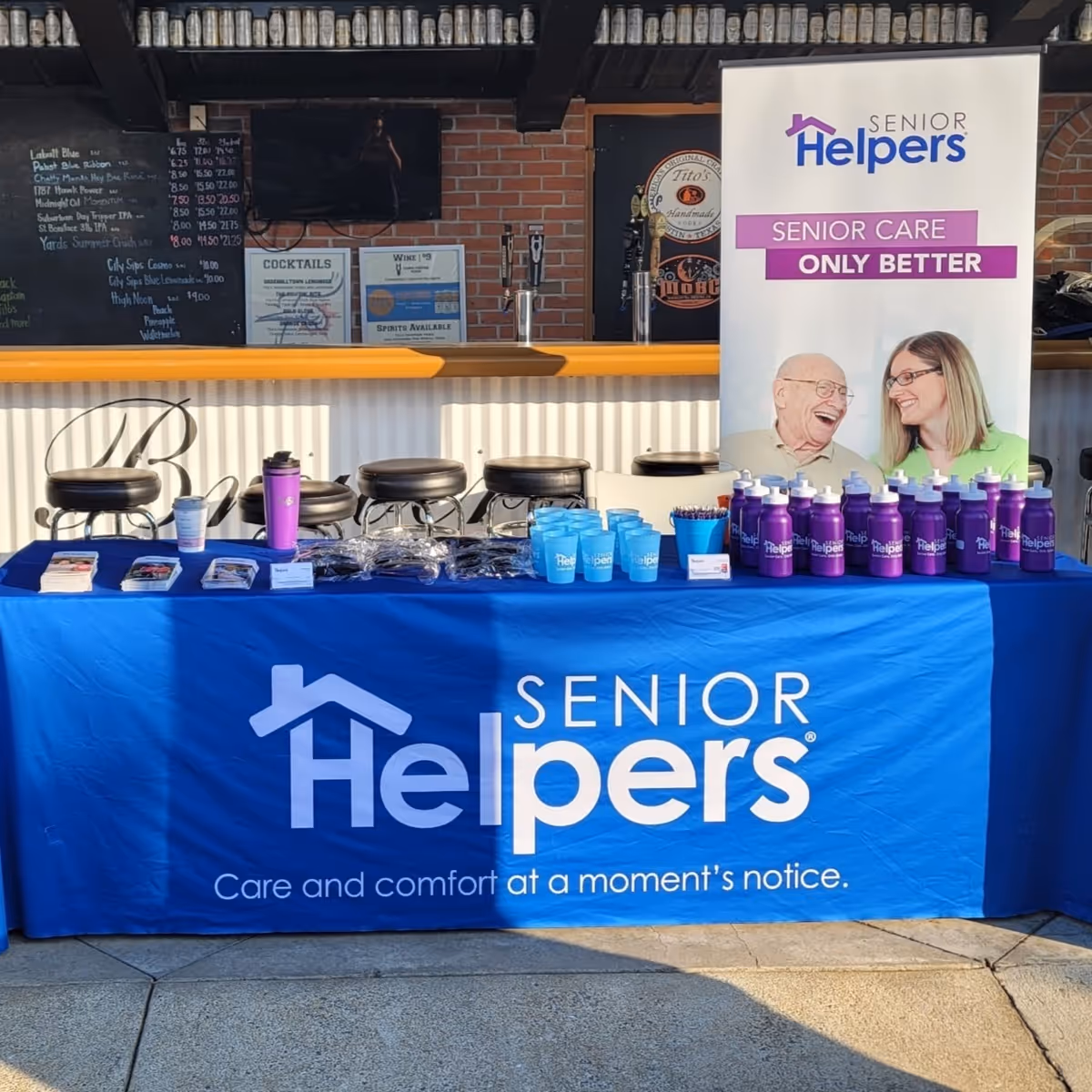 Promotional Senior Helpers booth with blue tablecloth and banner indoors.