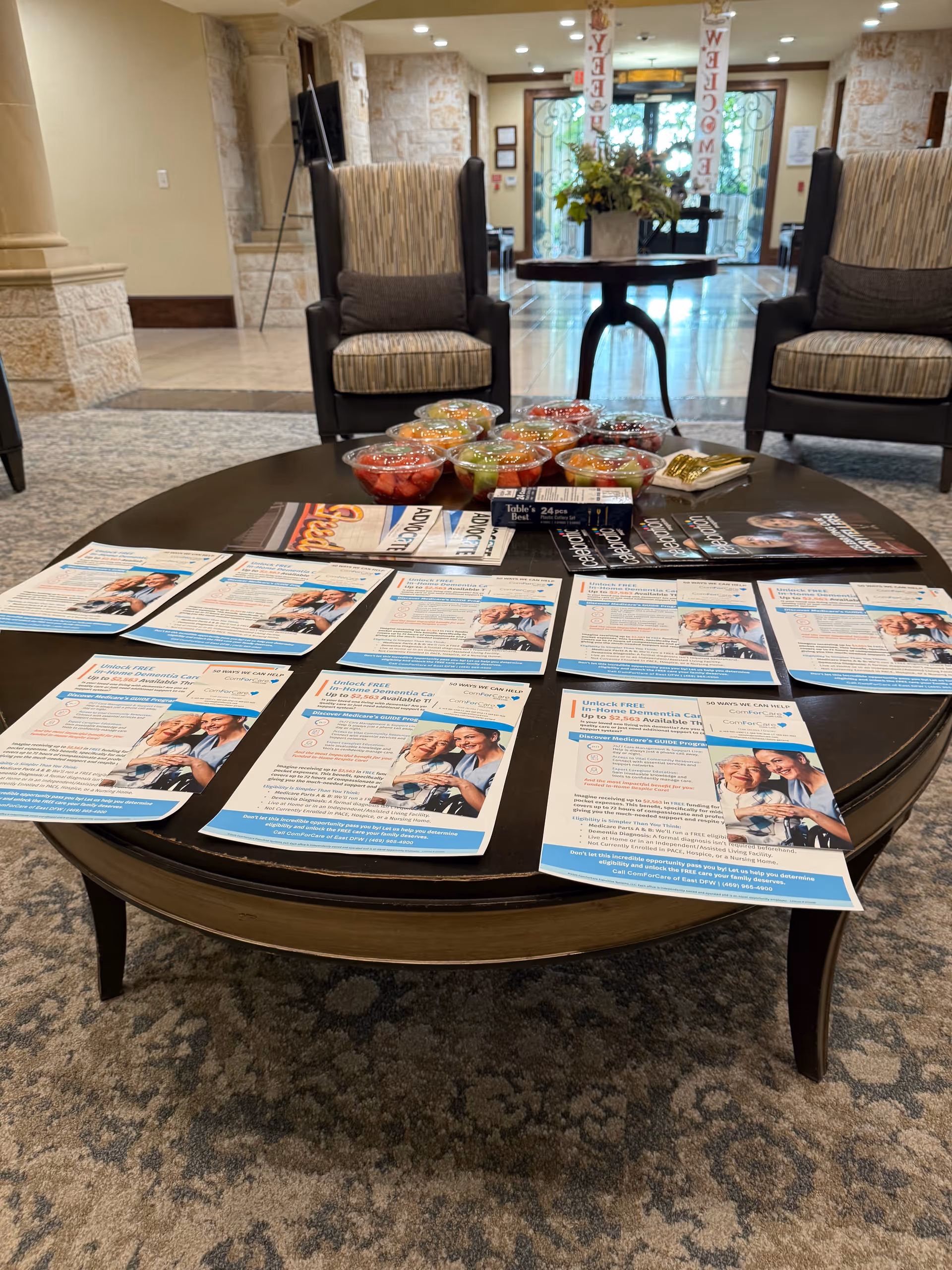 Round coffee table with flyers and bowls in a lobby area flanked by two armchairs.