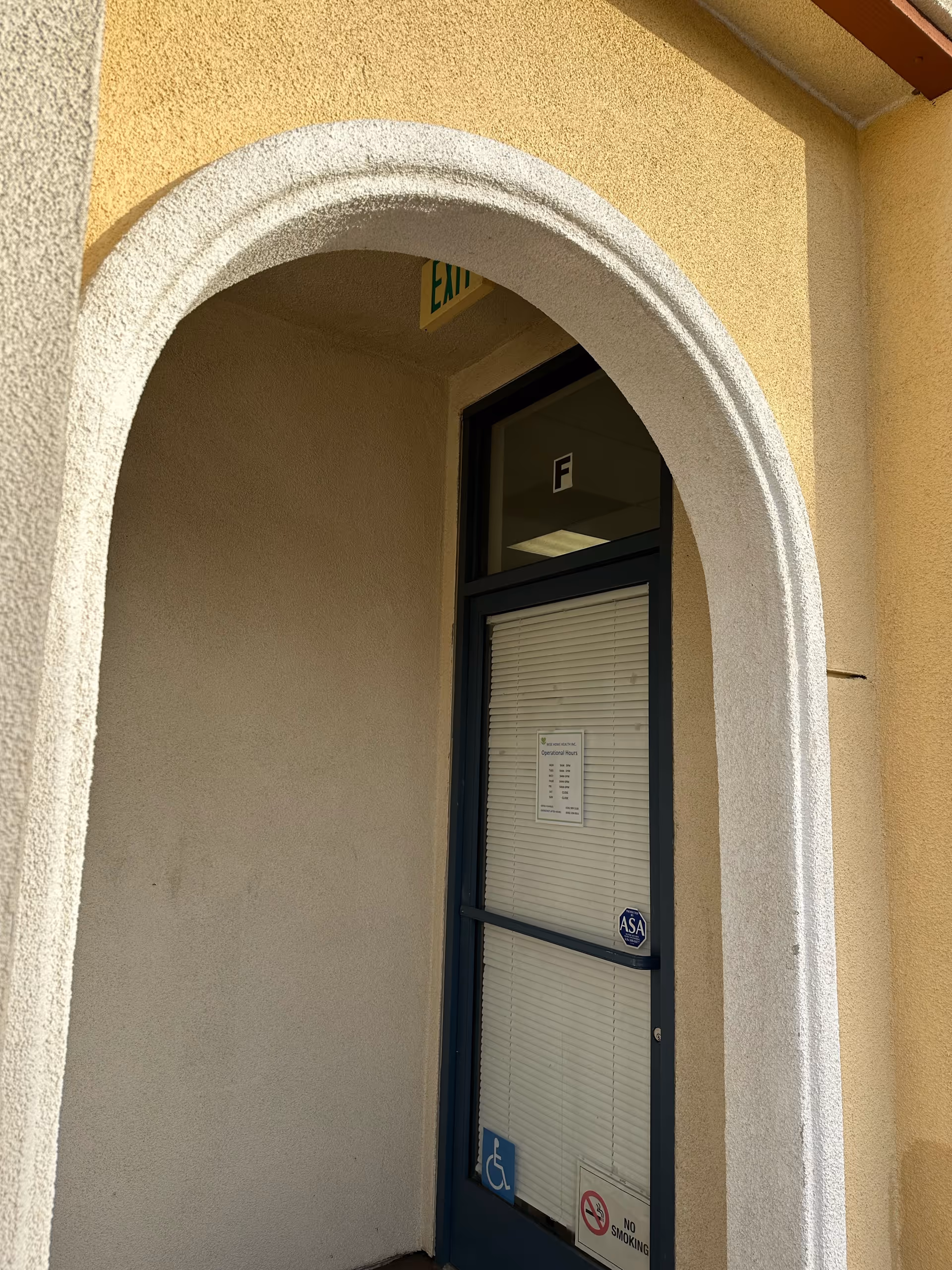 Arched exterior doorway with beige stucco walls and a blue-framed glass door labeled Exit