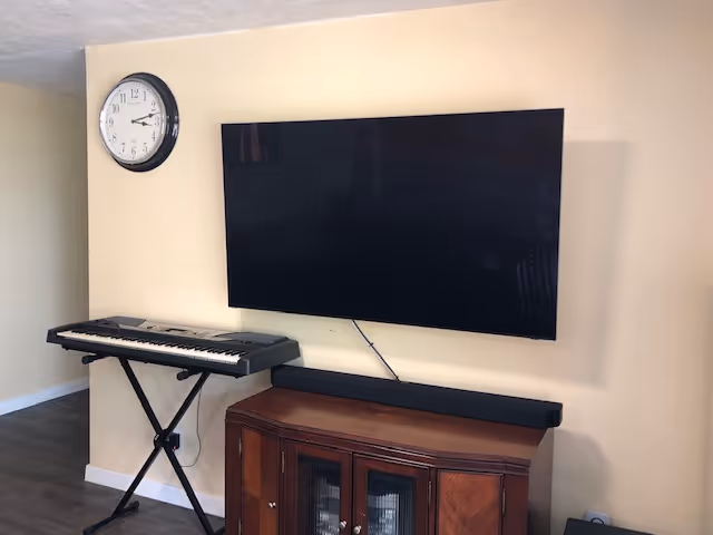 Living room area with mounted TV, keyboard, wall clock, and wooden cabinet.