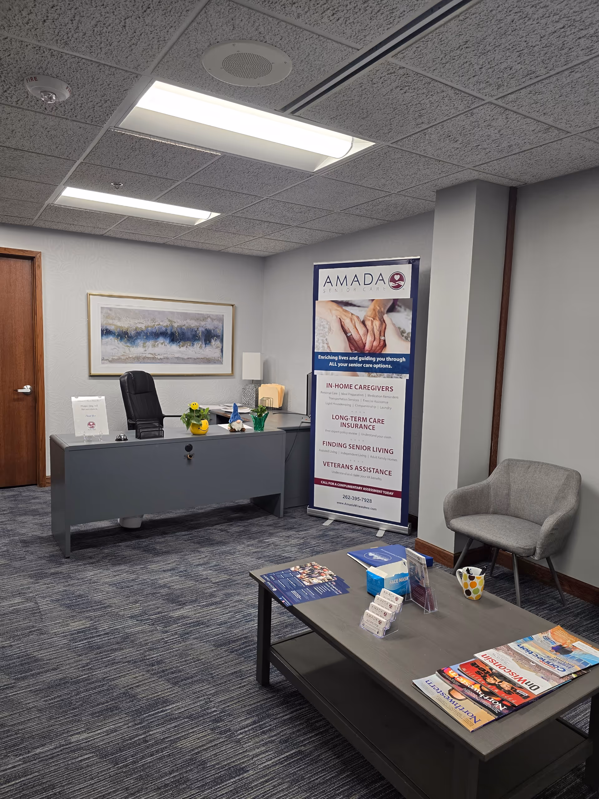 Reception area of an Amada Senior Care office with desk, banner, and seating.