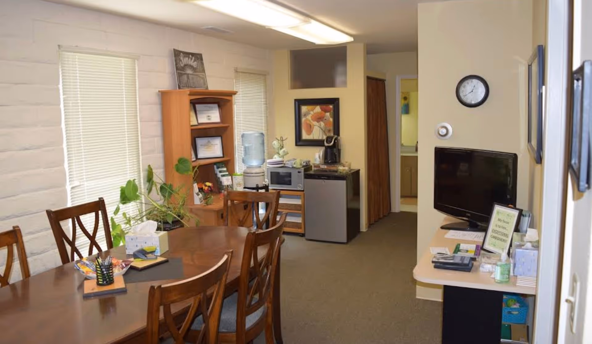 Common living area with a wooden dining table, chairs, kitchenette, and a television.