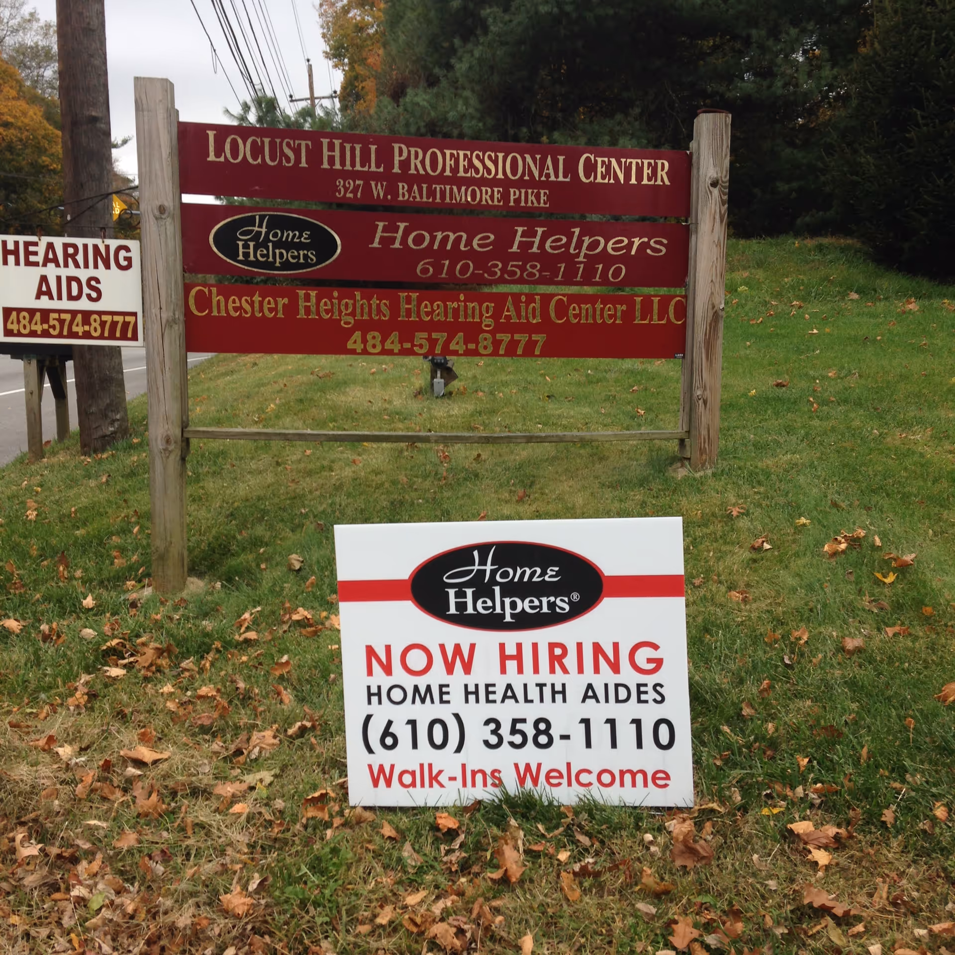 Outdoor grassy area with a large Locust Hill Professional Center sign and a Now Hiring sign.