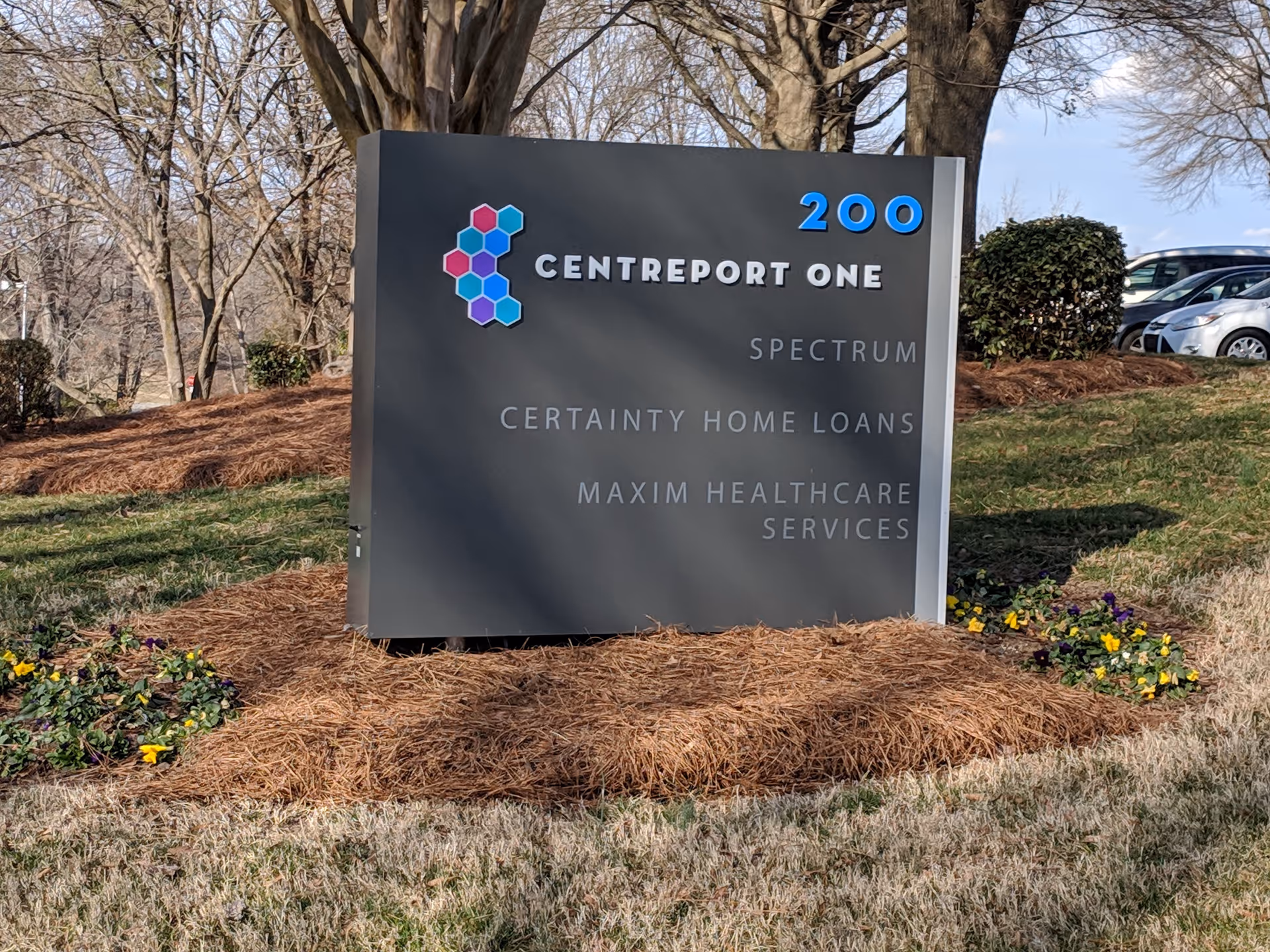 Outdoor sign with Maxim Healthcare Services and Centreport One, surrounded by mulch and plants.