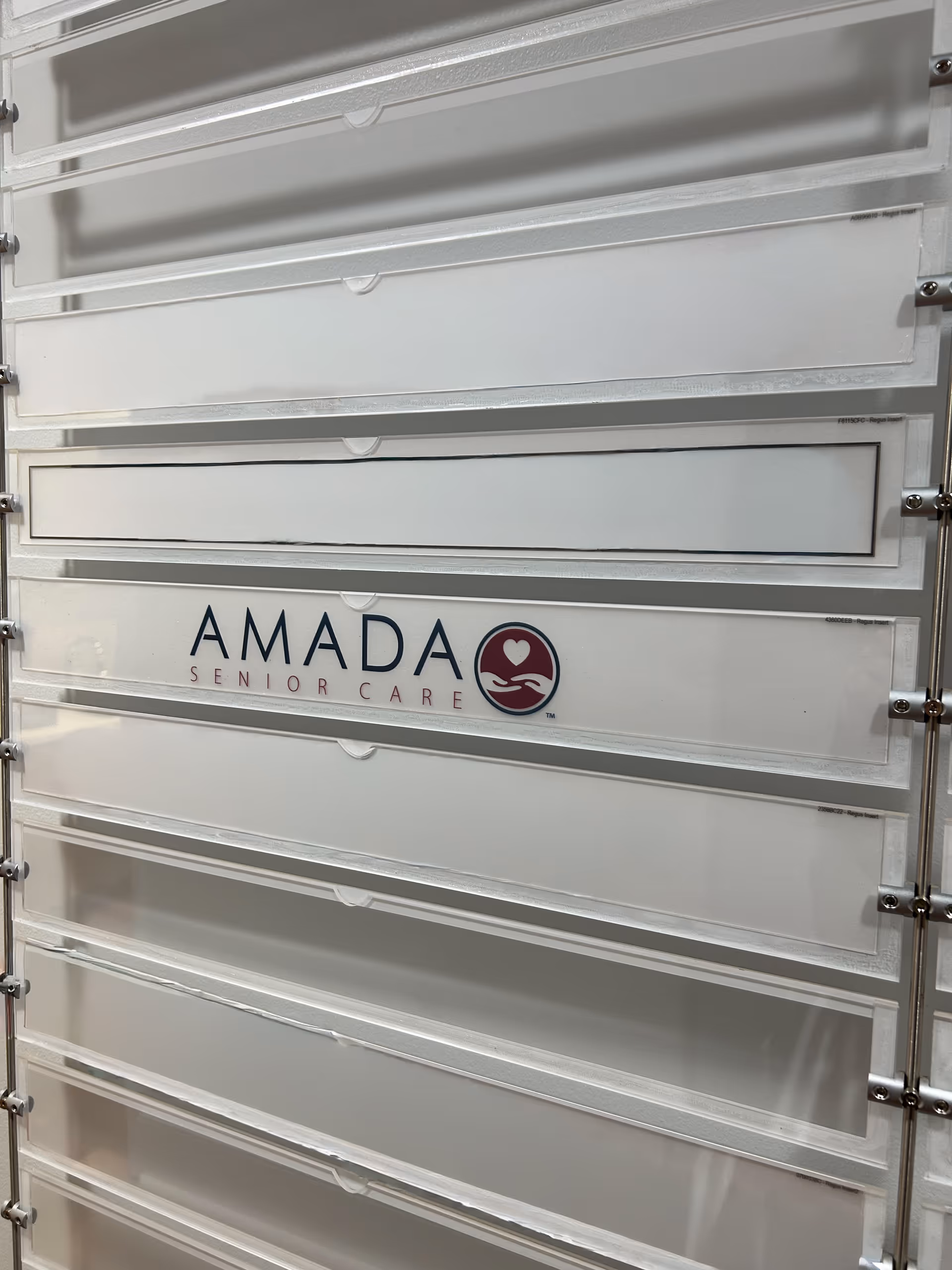 White metal mailbox lockers with Amada Senior Care logo in an interior hallway.