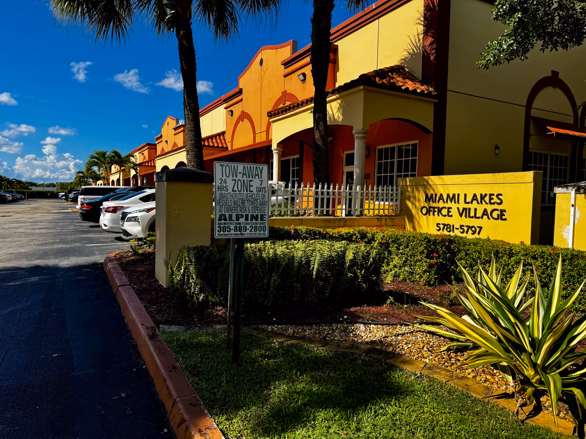 Colorful exterior of a yellow building with palm trees and the Miami Lakes Office Village sign.