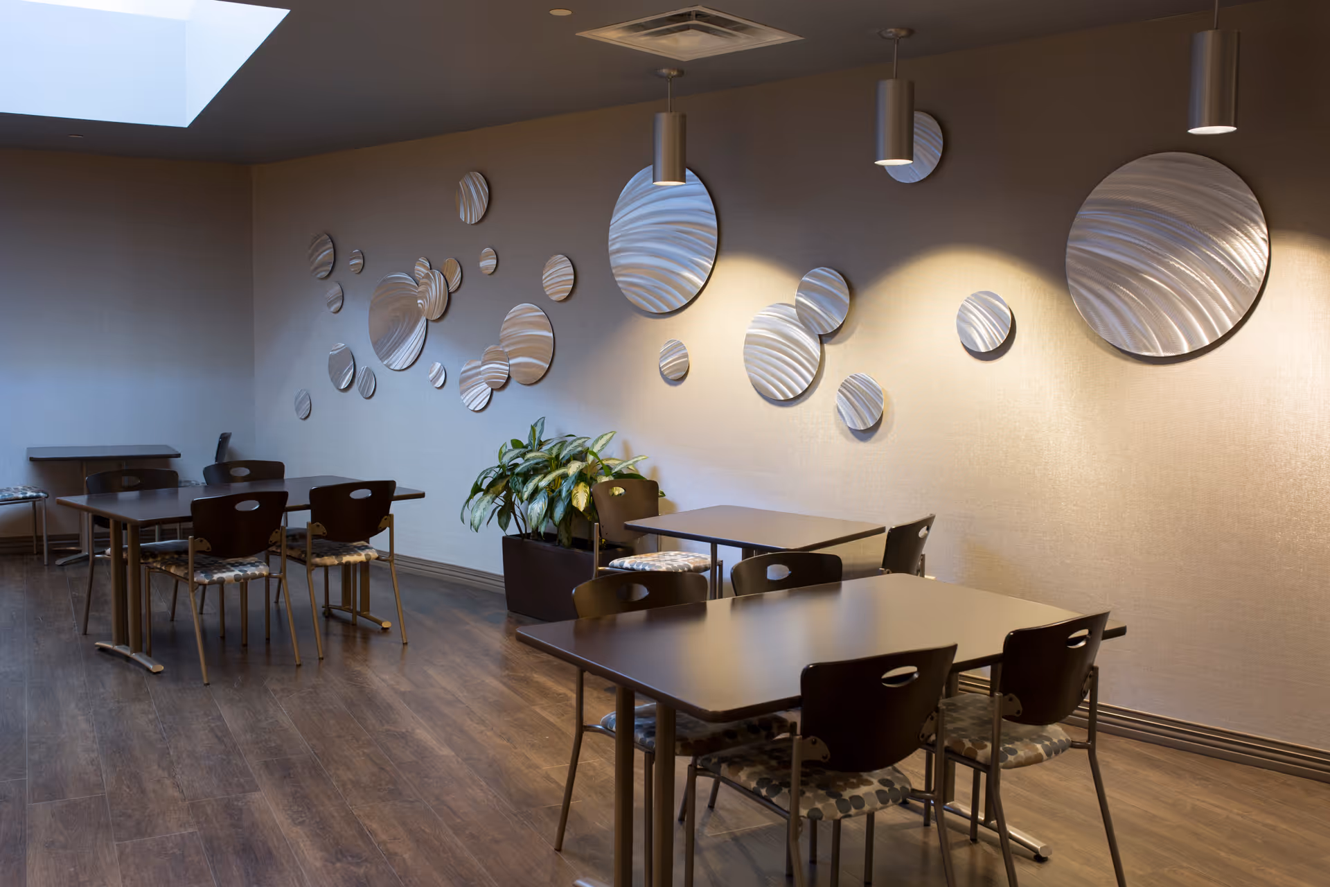 Interior dining area with multiple tables, chairs, and circular metal wall art.