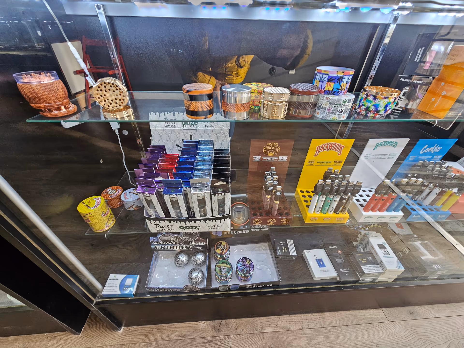 Glass display case showcases assorted smoking accessories and colorful packaging in a retail shop.