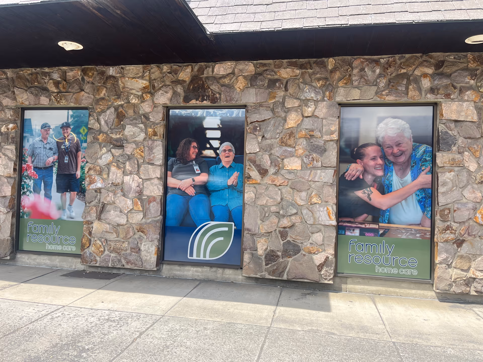 Stone-front building with three window displays featuring smiling people advertising Family Resource Home Care.