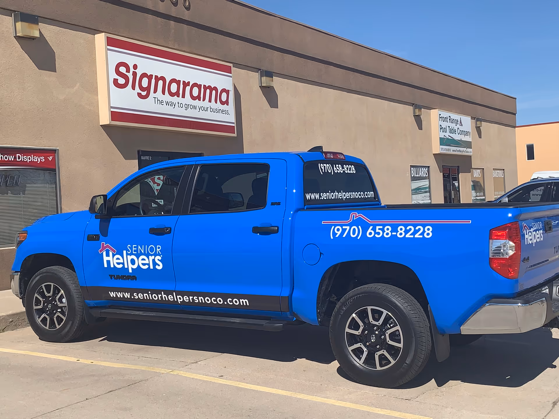 Blue Senior Helpers truck parked in front of a beige commercial building with Signarama sign.