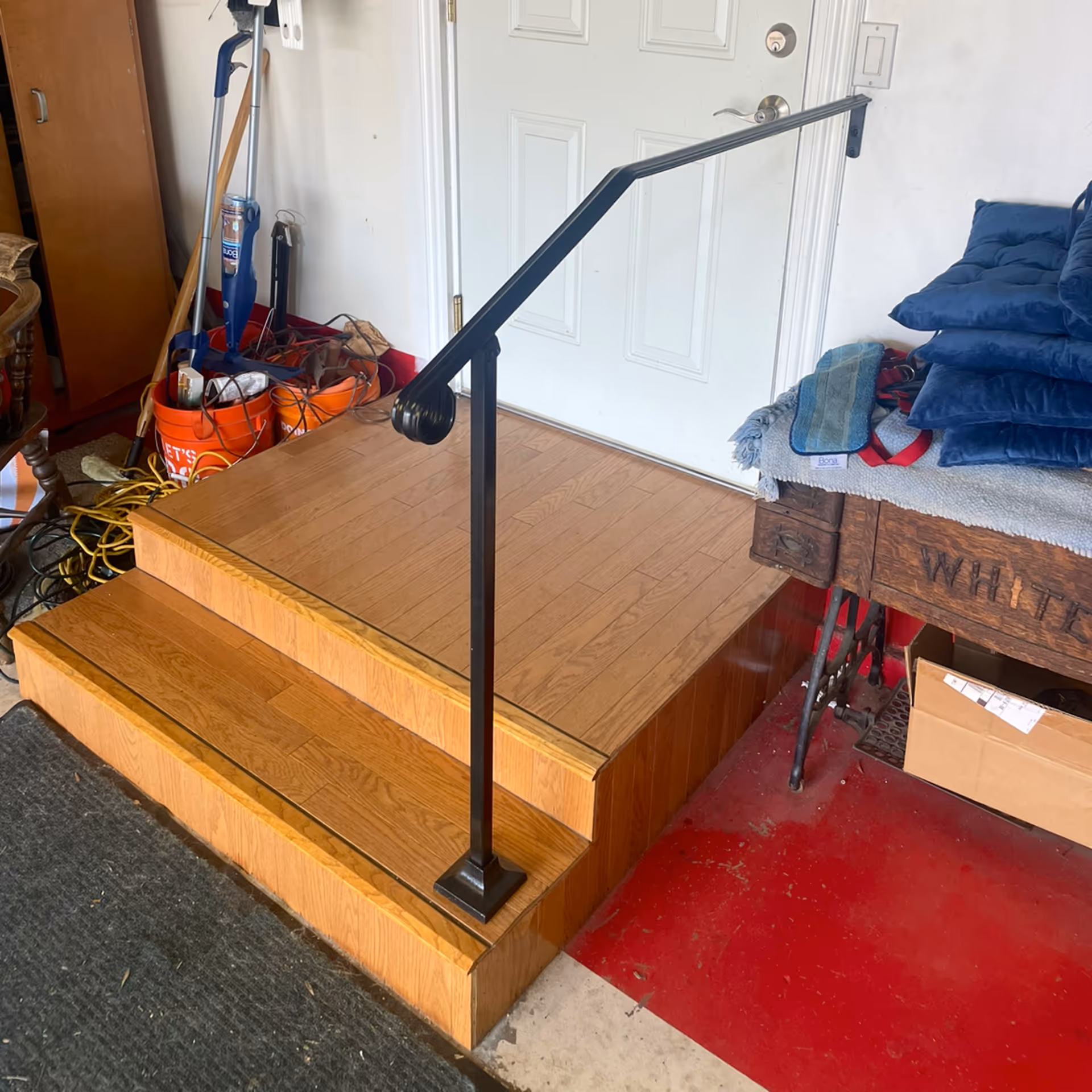 A black metal handrail runs along wooden steps beside a cluttered entry.