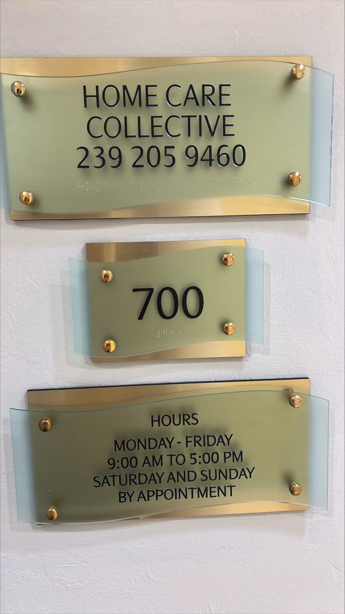 Interior wall with frosted glass signs displaying Home Care Collective, phone number, suite 700, and hours.