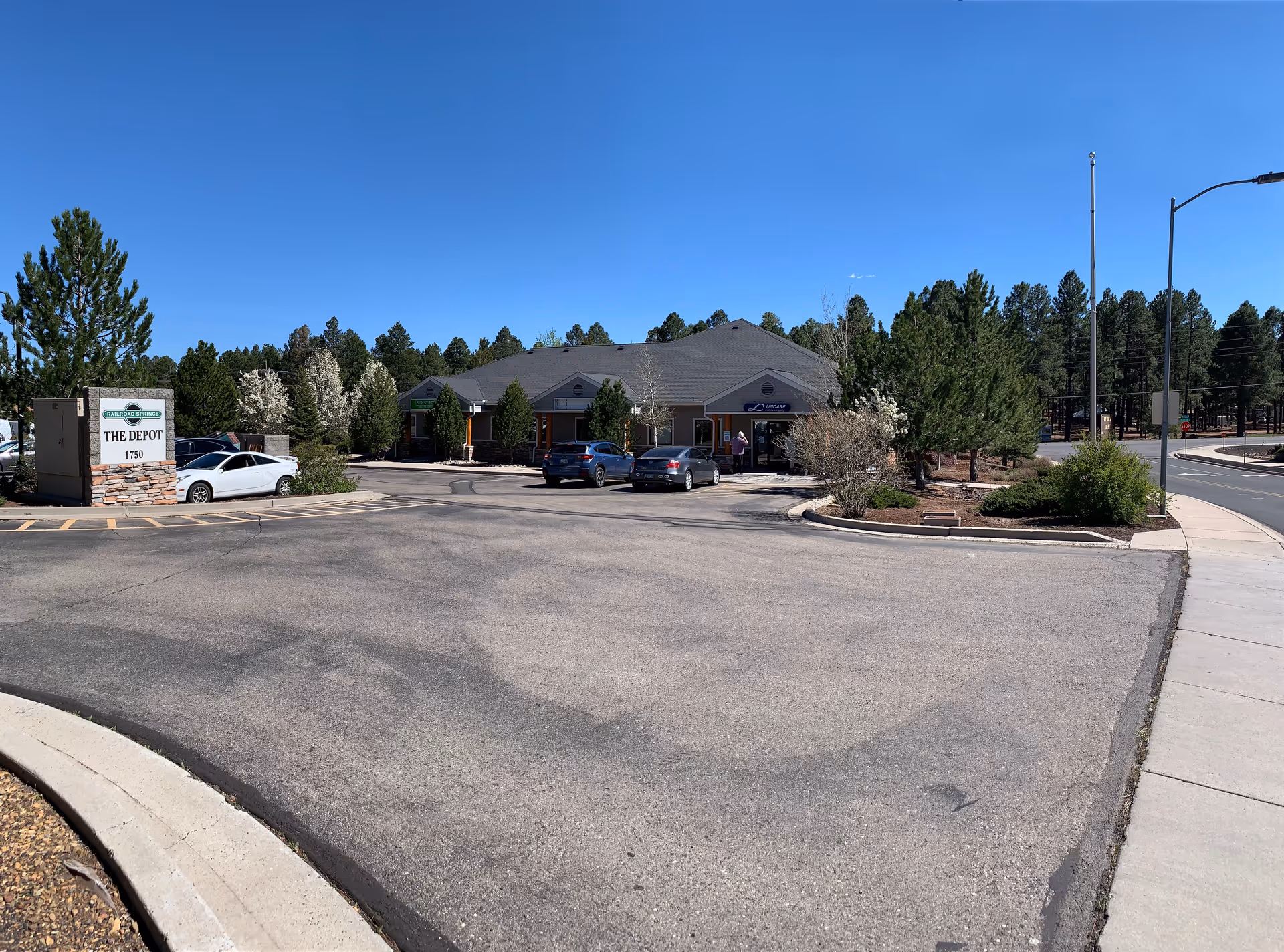 Exterior view of a single-story senior living facility with a parking lot and surrounding trees.