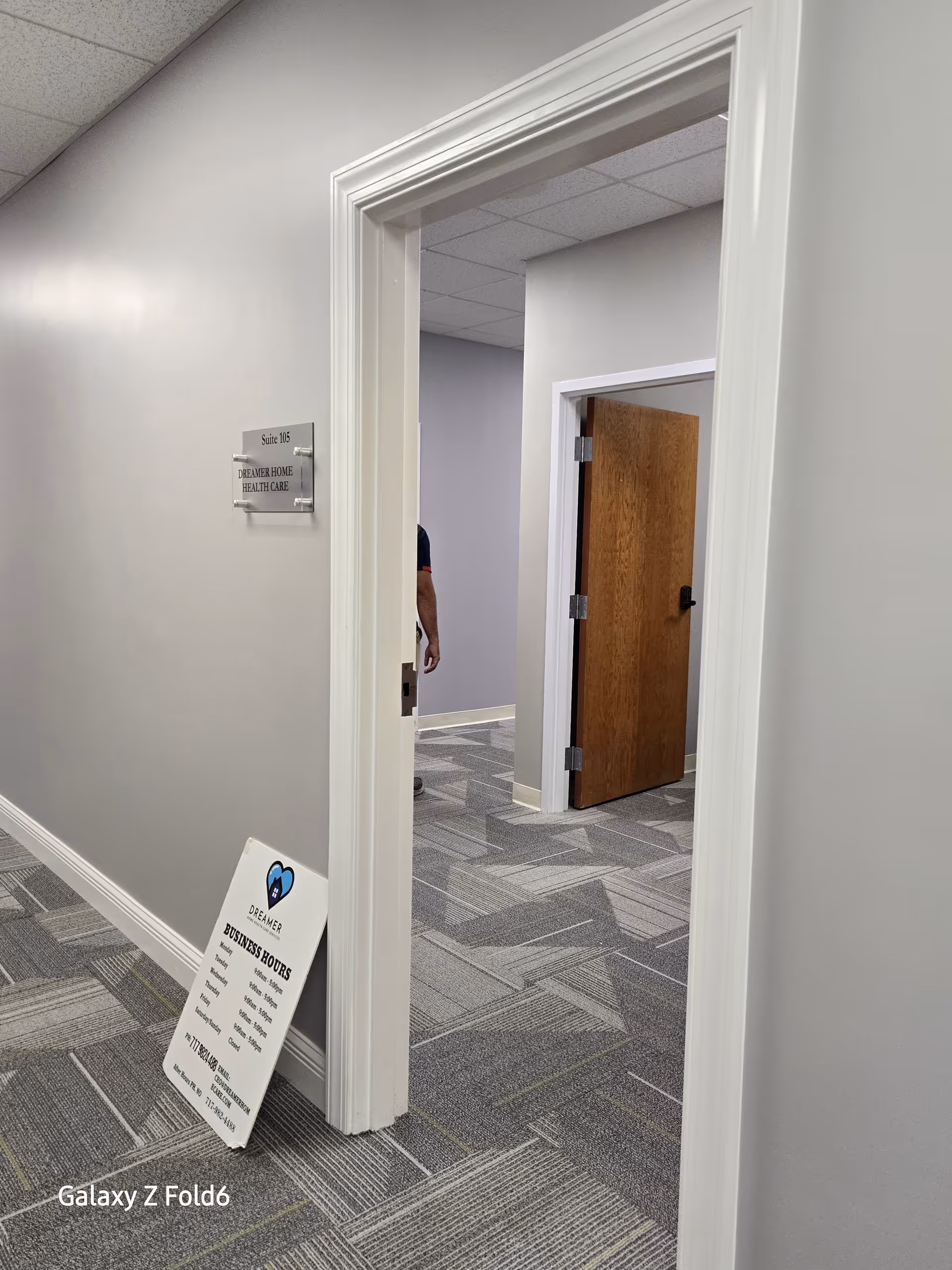 Interior hallway of a senior living facility with doorways, signage, and a partially visible person.