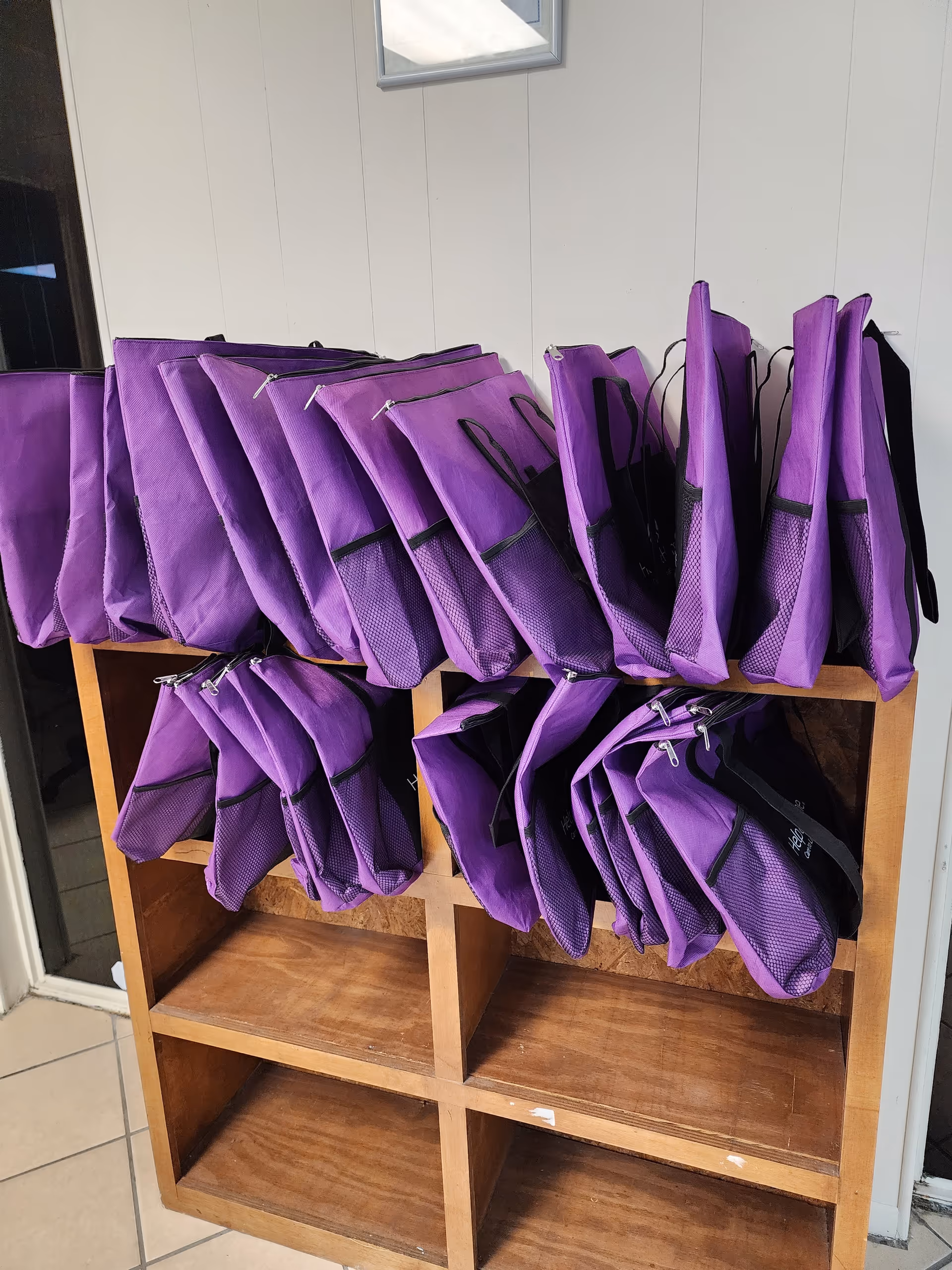 Purple bags hang on a wooden cubby shelf inside Help at Home facility.