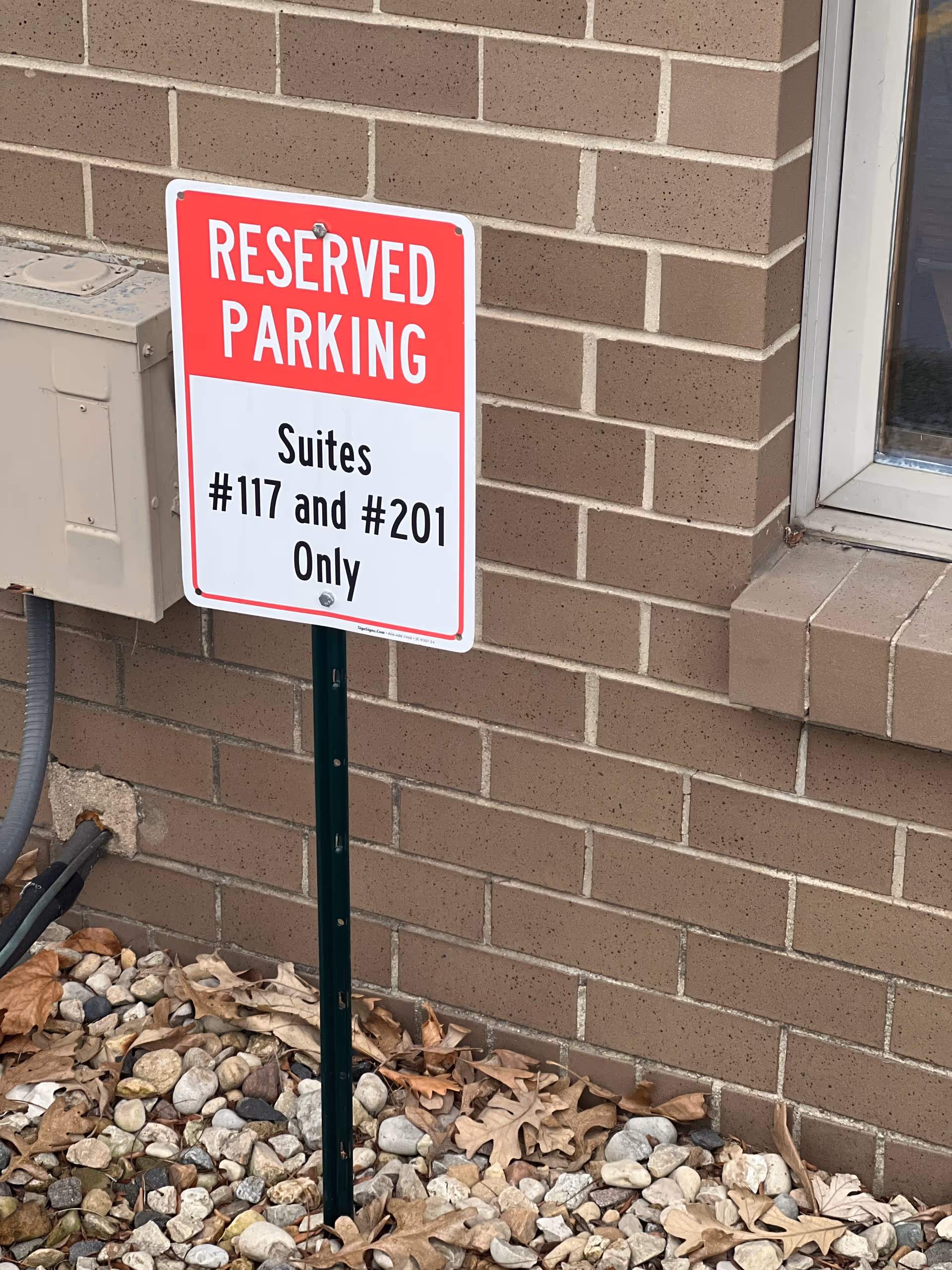 Red and white Reserved Parking sign on brick building exterior near rocks