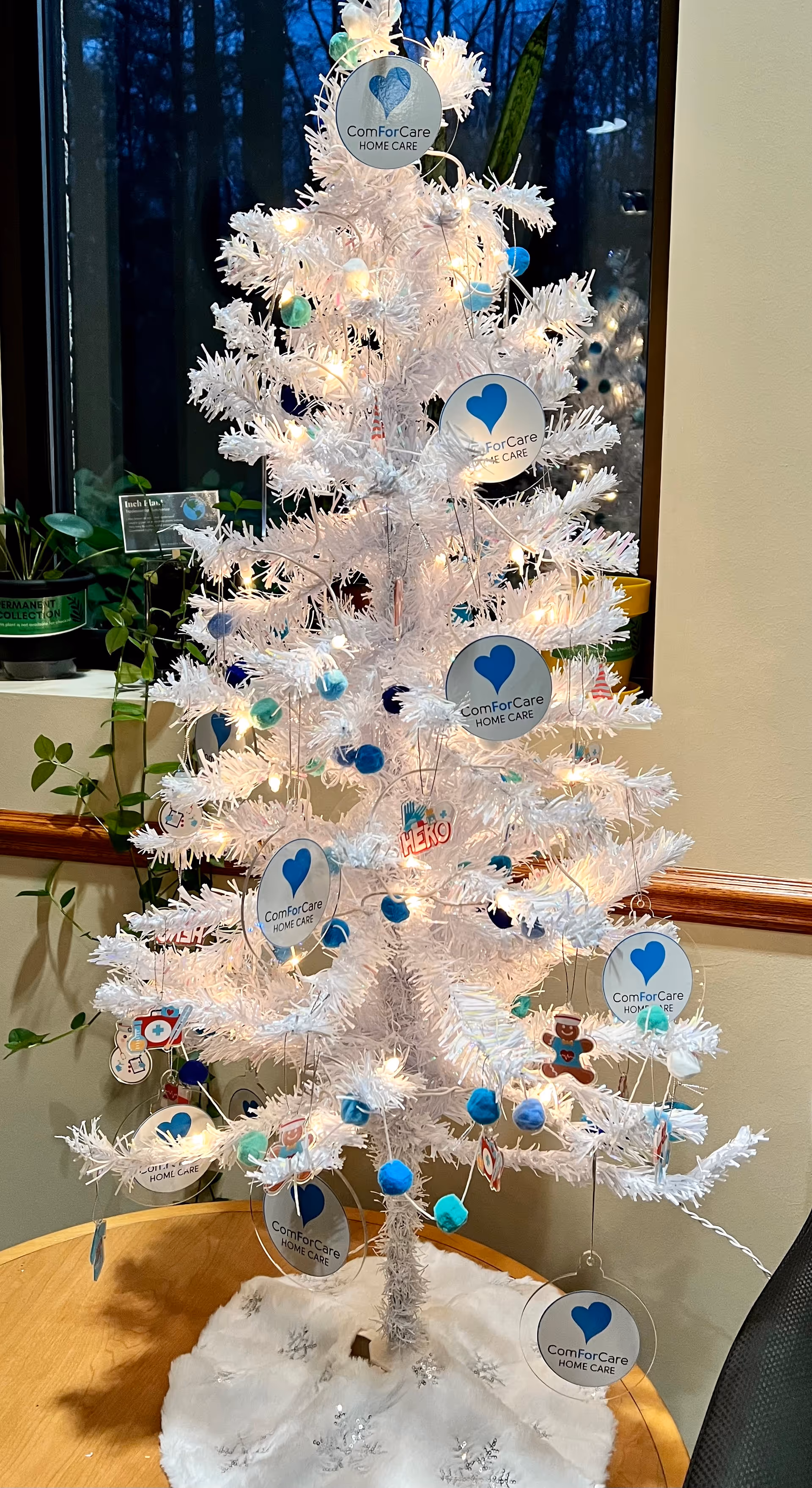 White artificial Christmas tree with ComForCare tags in a facility lobby.