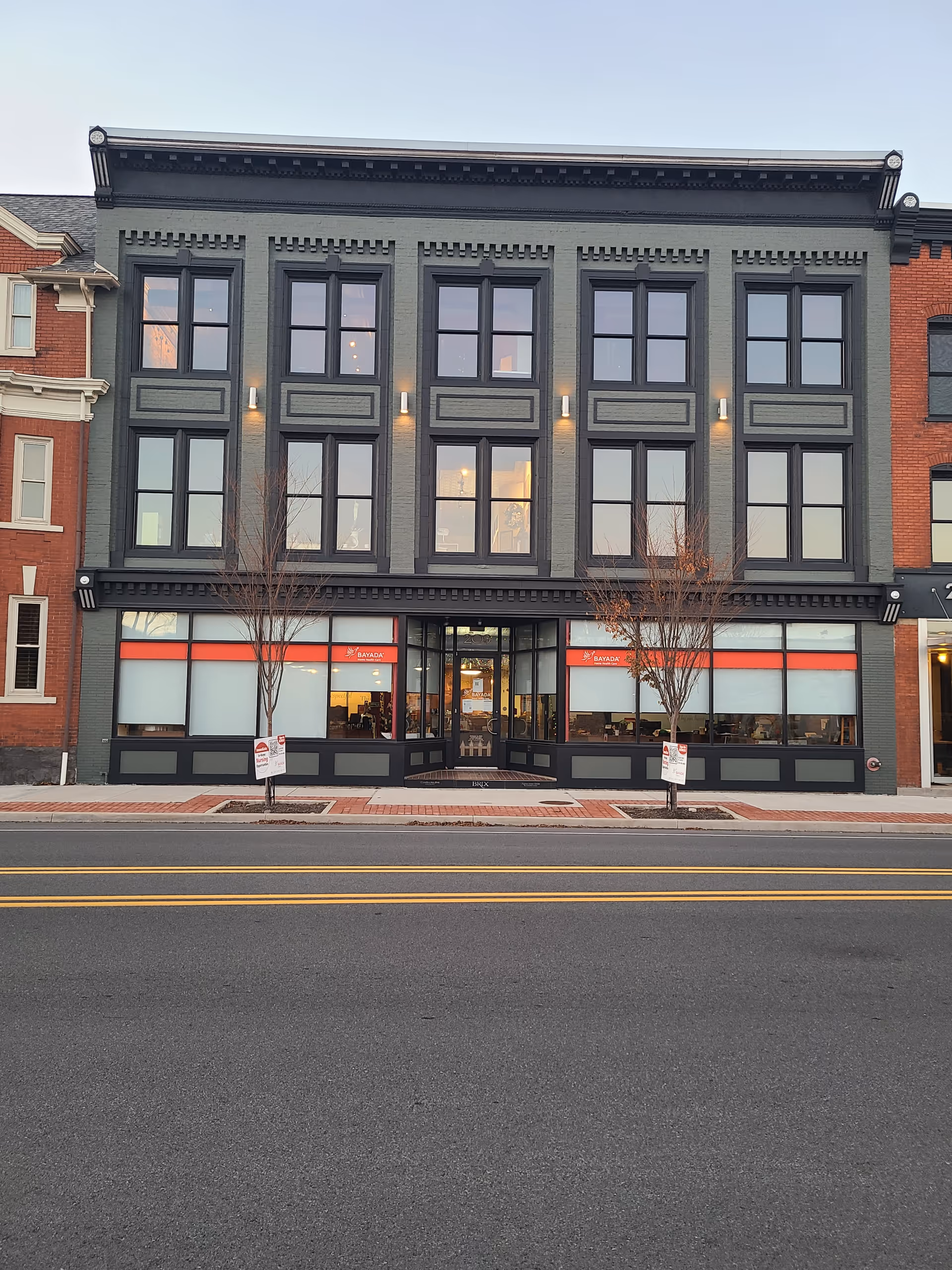 Three-story gray brick building with BAYADA Home Health storefront windows along a city street.