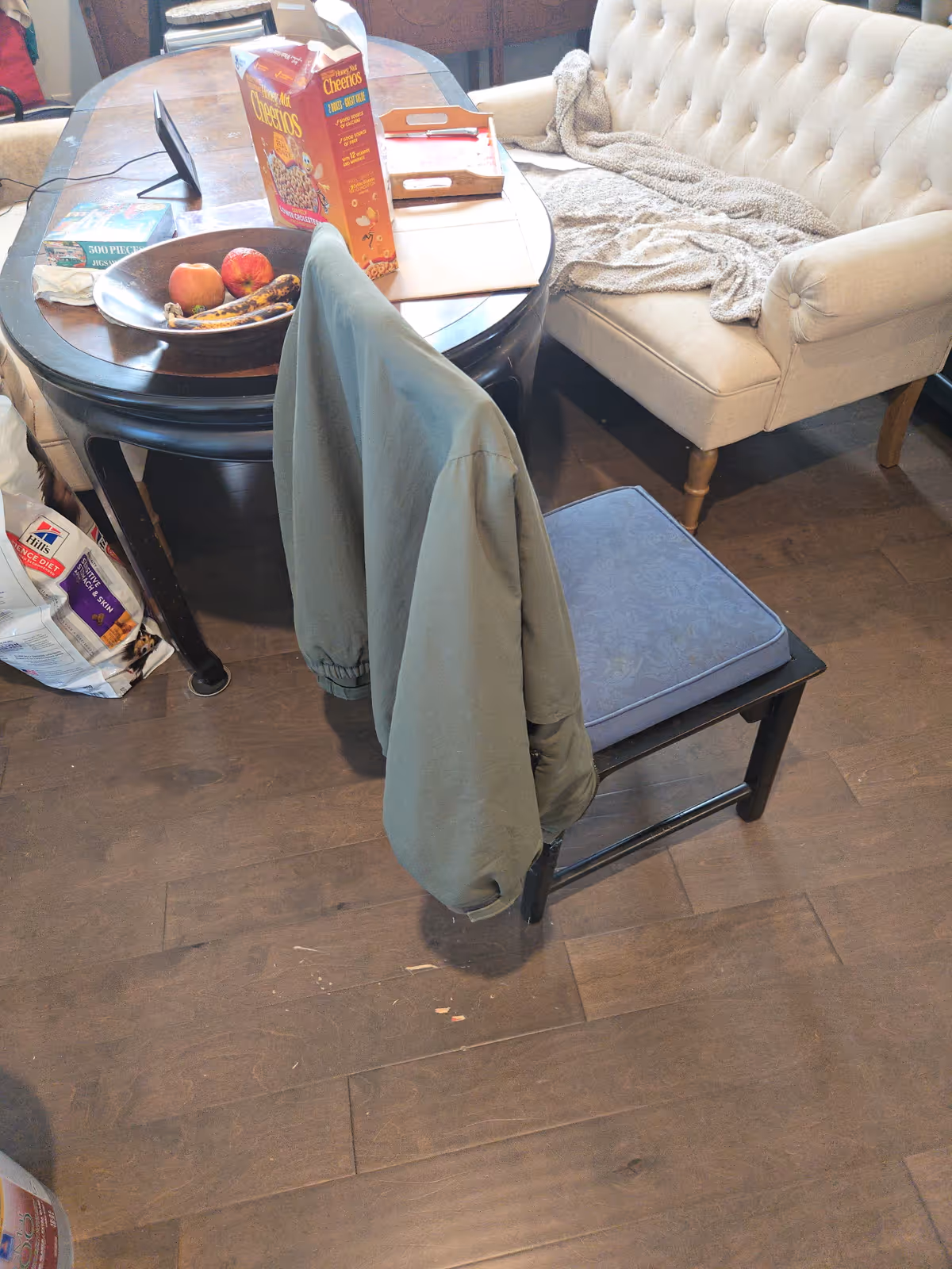 Cozy interior common area with round table, jacket on chair, sofa, fruit bowl, and cereal box.