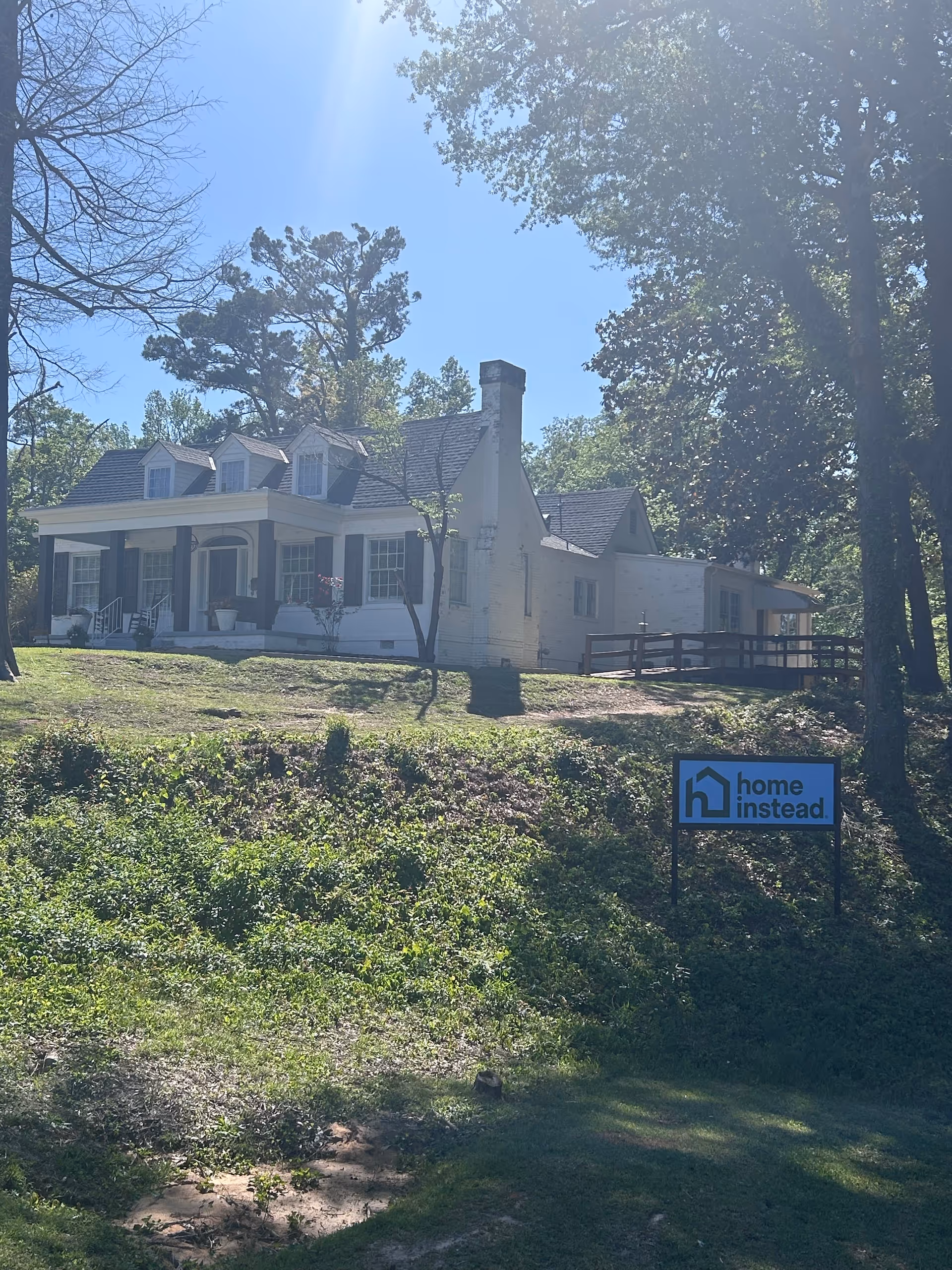 Exterior view of a white, ranch-style senior living home with a Home Instead sign.