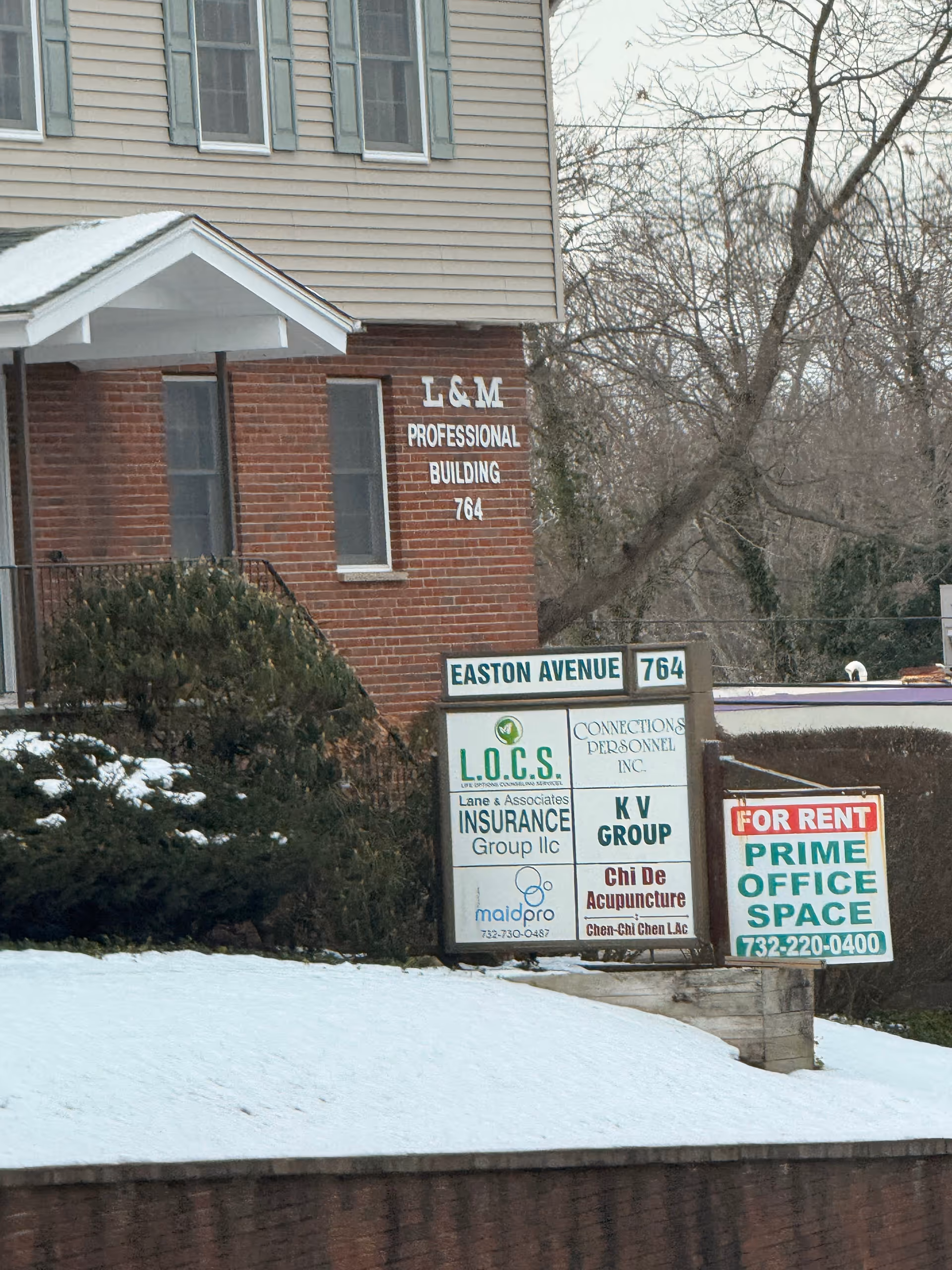 Exterior view of a two-story building with brick base and office signs.