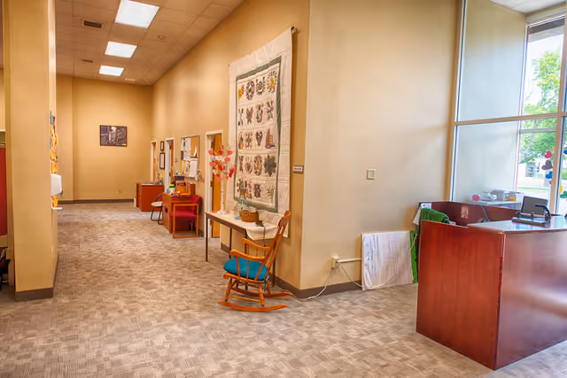 Interior hallway of a senior living facility with quilts on walls and a reception desk