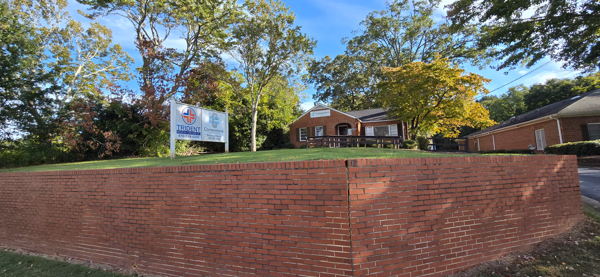 Brick building on a grassy hill behind a brick retaining wall and sign.