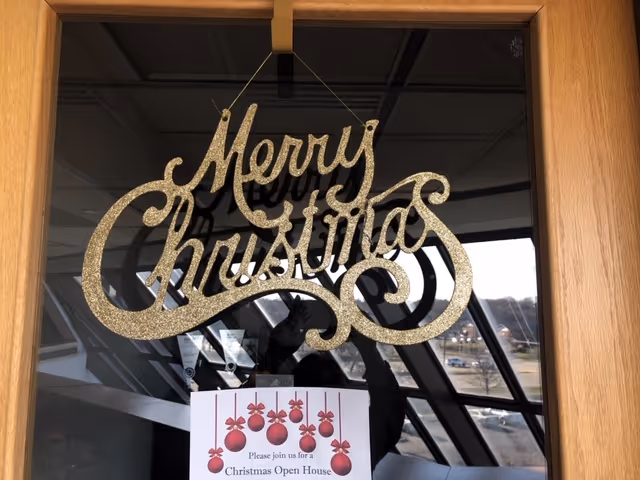 Glittery 'Merry Christmas' sign hanging on glass doors inside a senior living facility.