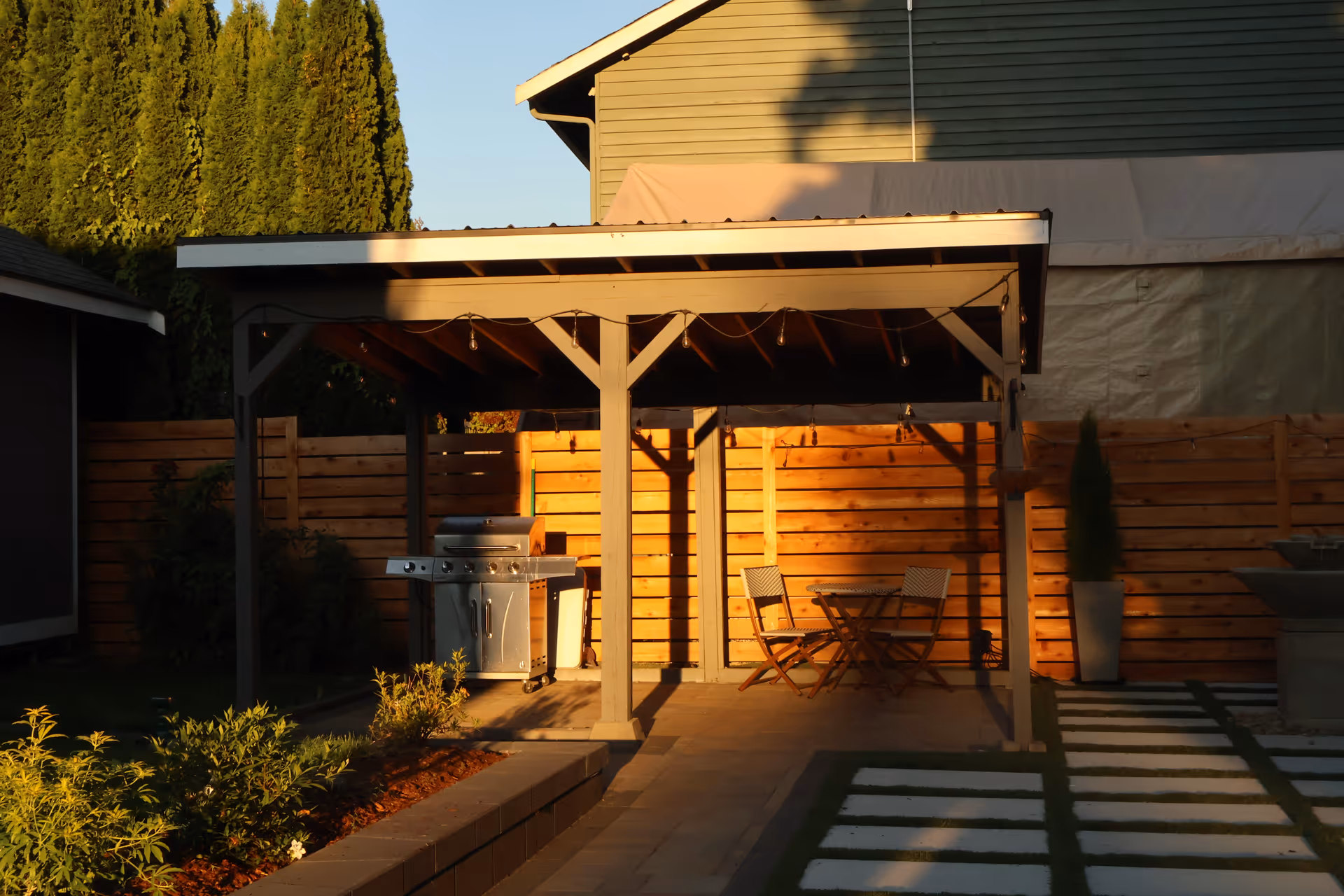 Outdoor patio with grill, table and chairs under a covered wooden structure.