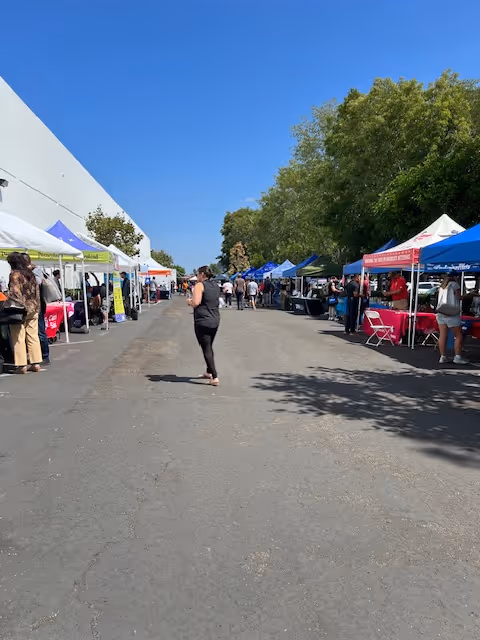 Outdoor market scene with tents and people walking along a sunny street.