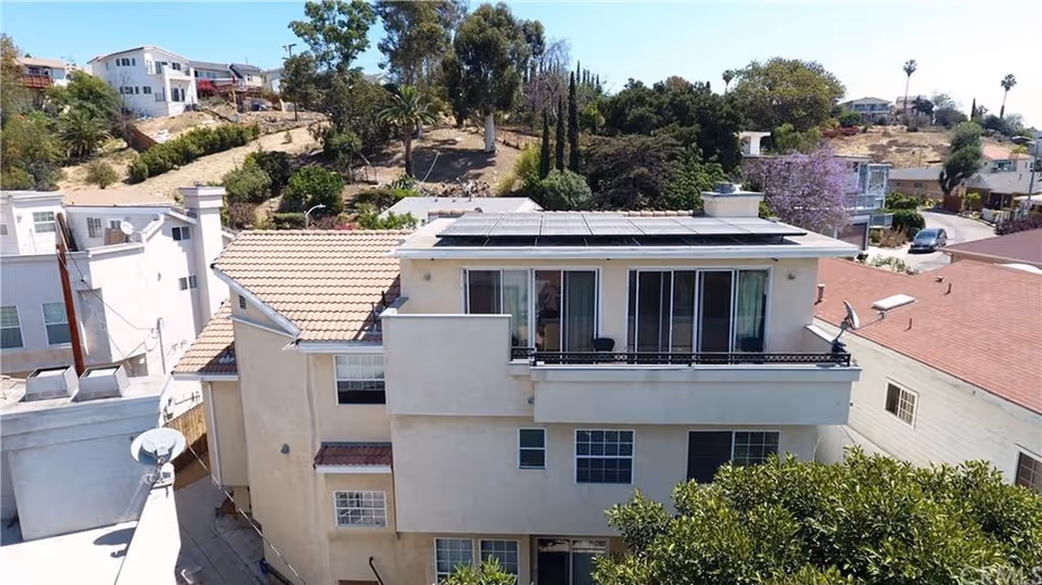 A multi-story residential building with solar panels on the roof, surrounded by trees.