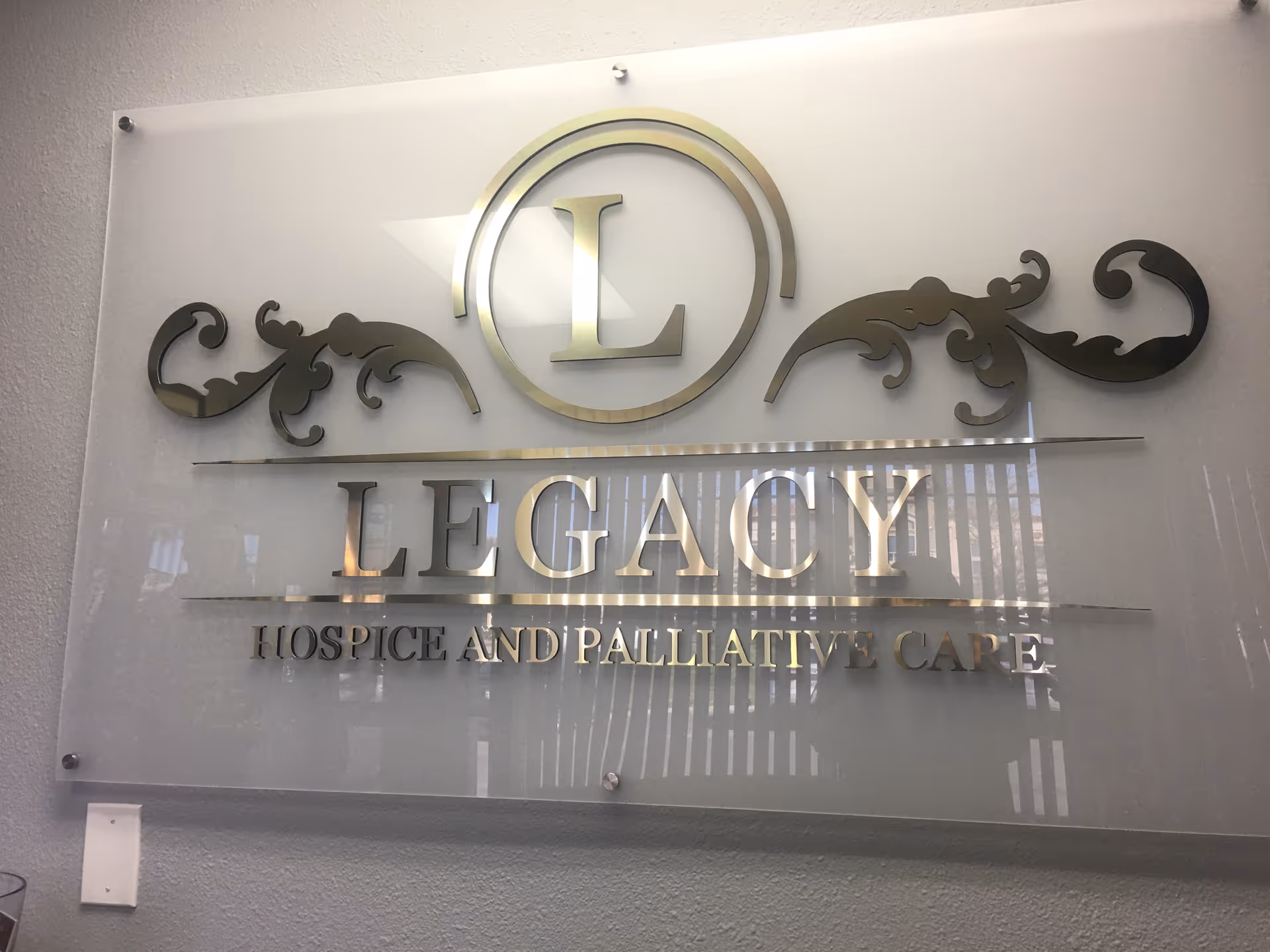 Interior glass plaque signage reading 'Legacy Hospice and Palliative Care' with decorative metal scrollwork.
